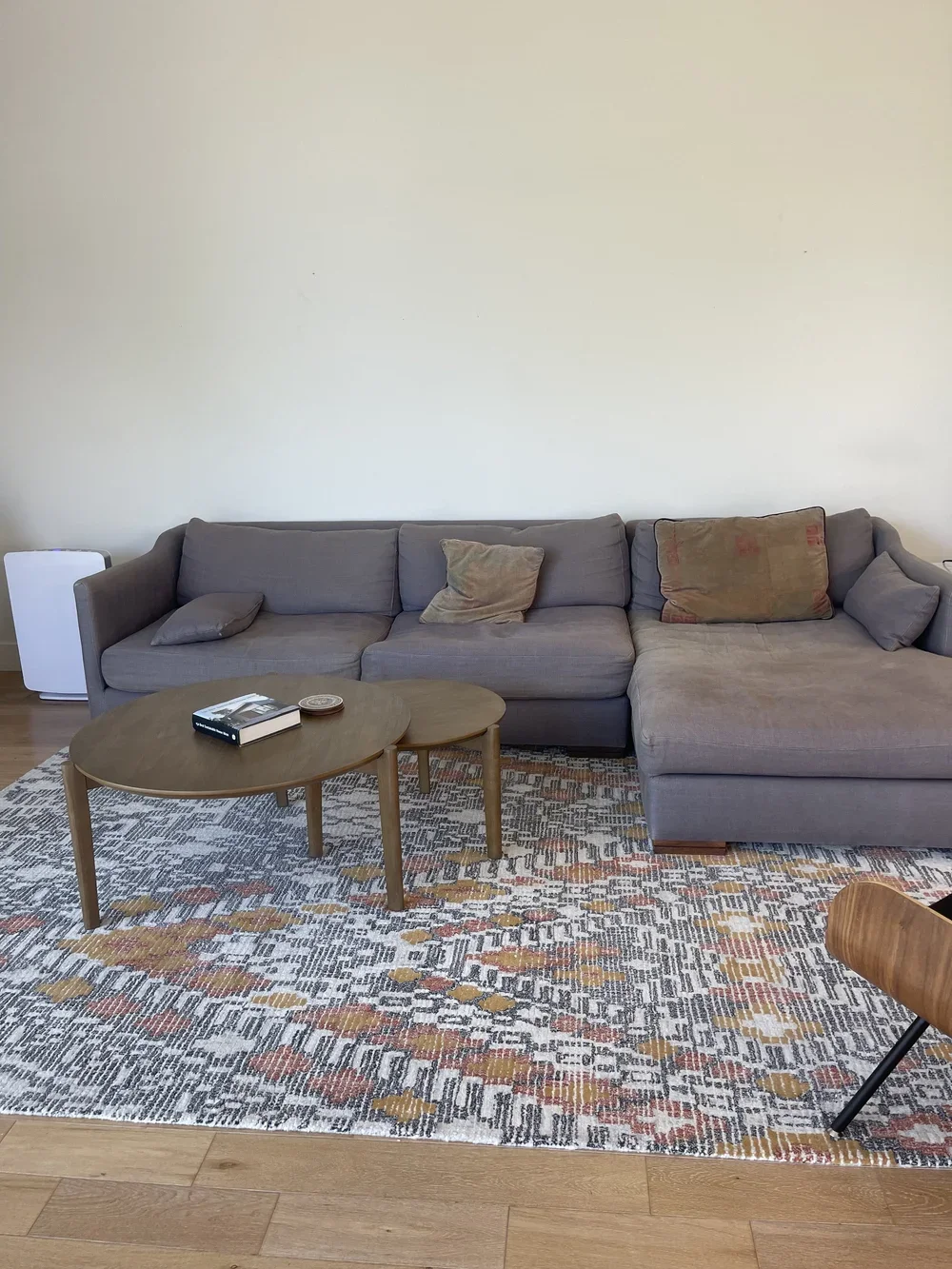 Living room with a gray sectional sofa, throw pillows, a wooden coffee table, a patterned area rug, and a white heater.