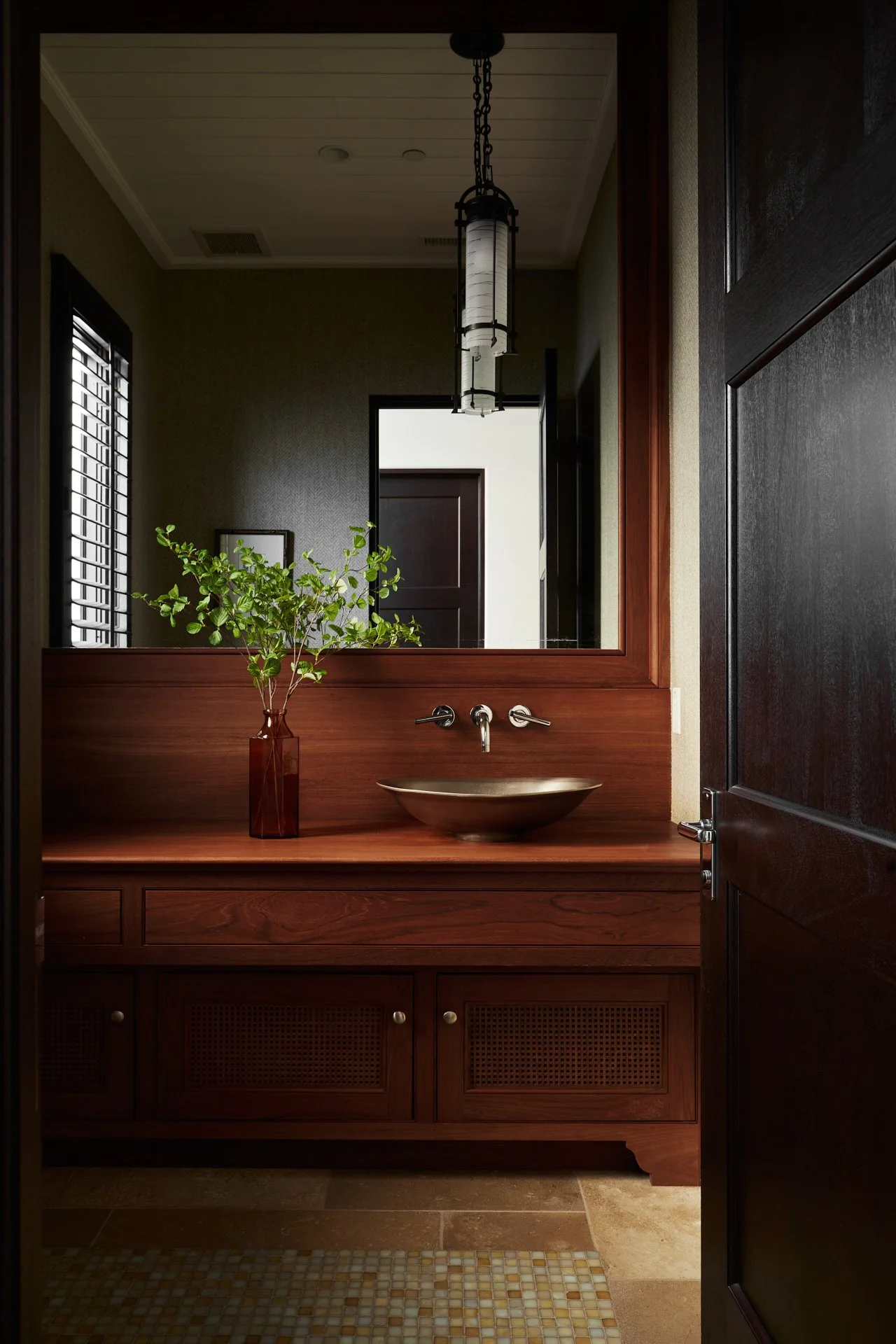 A bathroom vanity with a wooden countertop, a vessel sink, a large mirror, a vase with green leaves, and a pendant light fixture above.