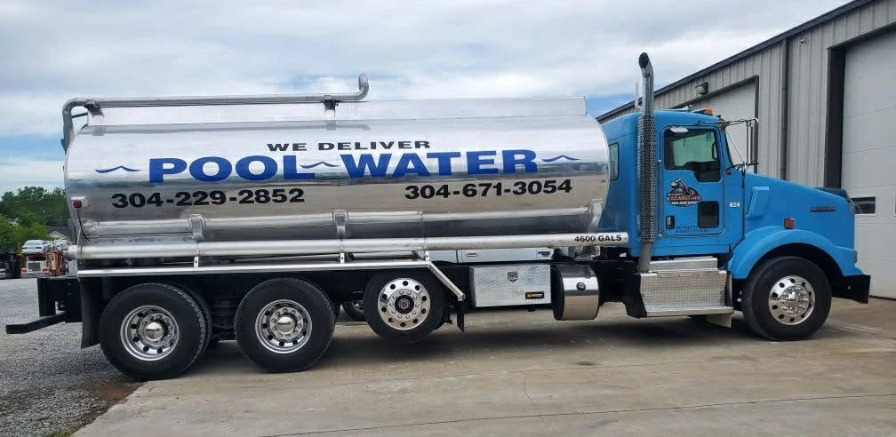 A large blue water delivery truck parked outside a building, with the words "We Deliver POOL WATER" and contact phone numbers on its tank.