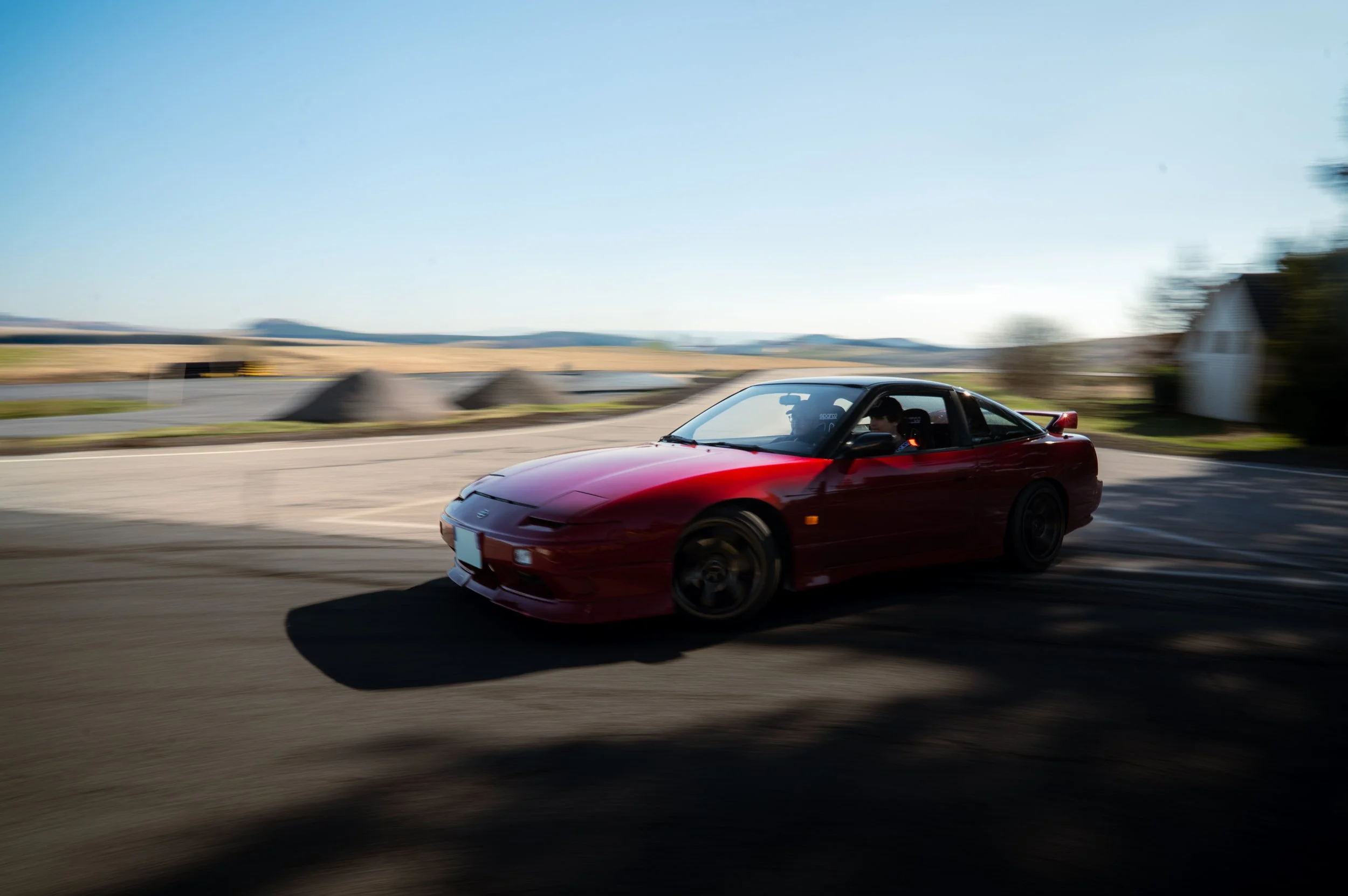 Red Nissan Silvia S13 driving on a rural road with motion blur in the background