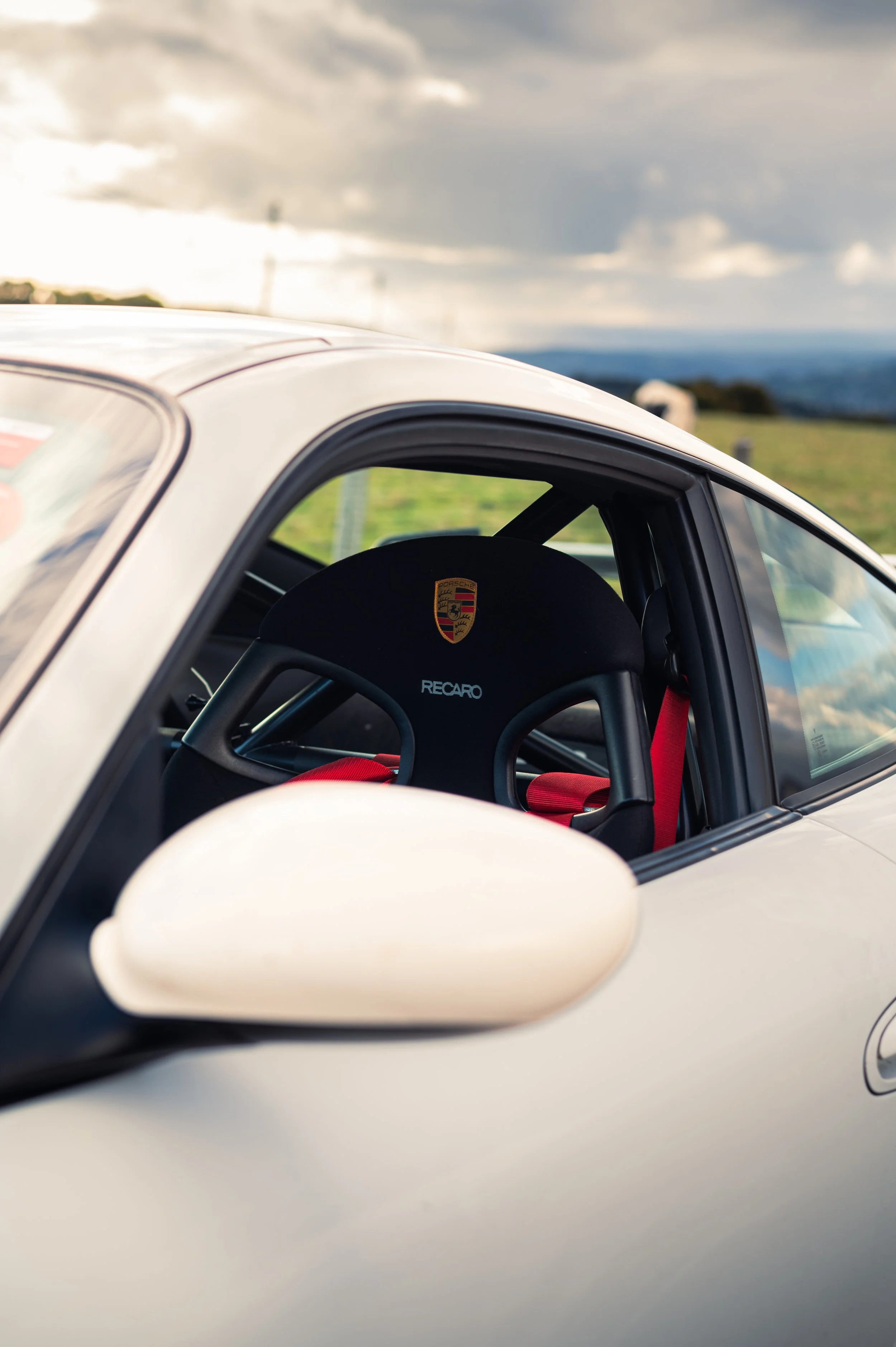 Close-up of a Porsche 911 (996) GT3 Clubsport in Clermont-Ferrand, with a scenic countryside background and cloudy sky.