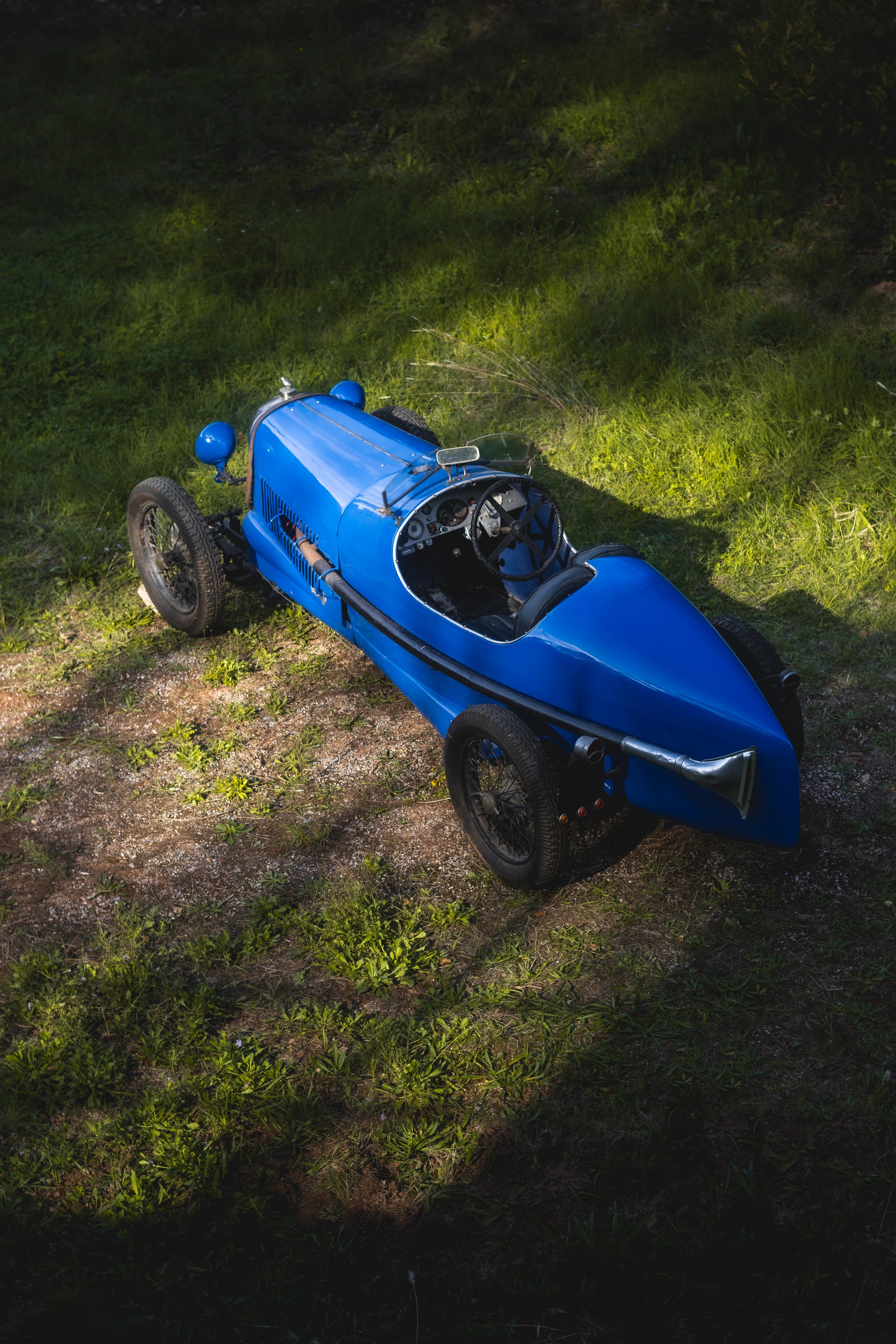 A vintage blue Salmson San Sebastián parked on grassy ground with sunlight and shadow patches.