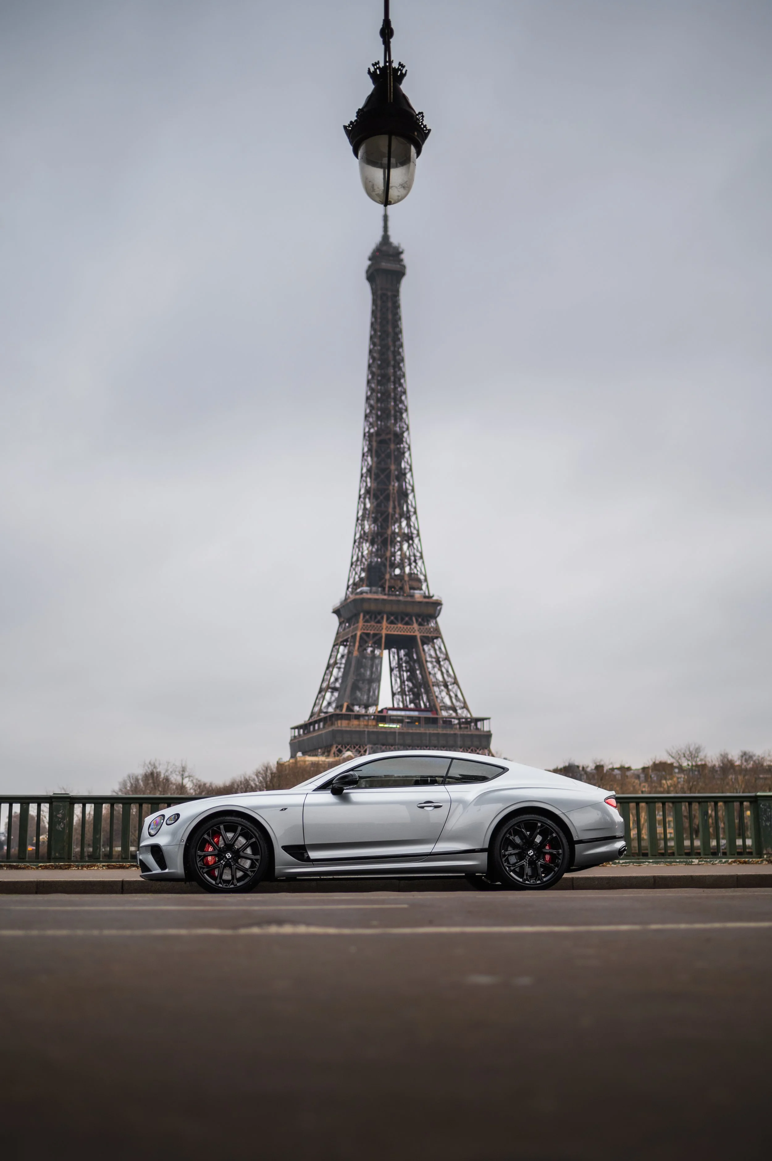 A silver Bentley Continental GT V8S parked on the street in front of the Eiffel Tower in Paris, France.