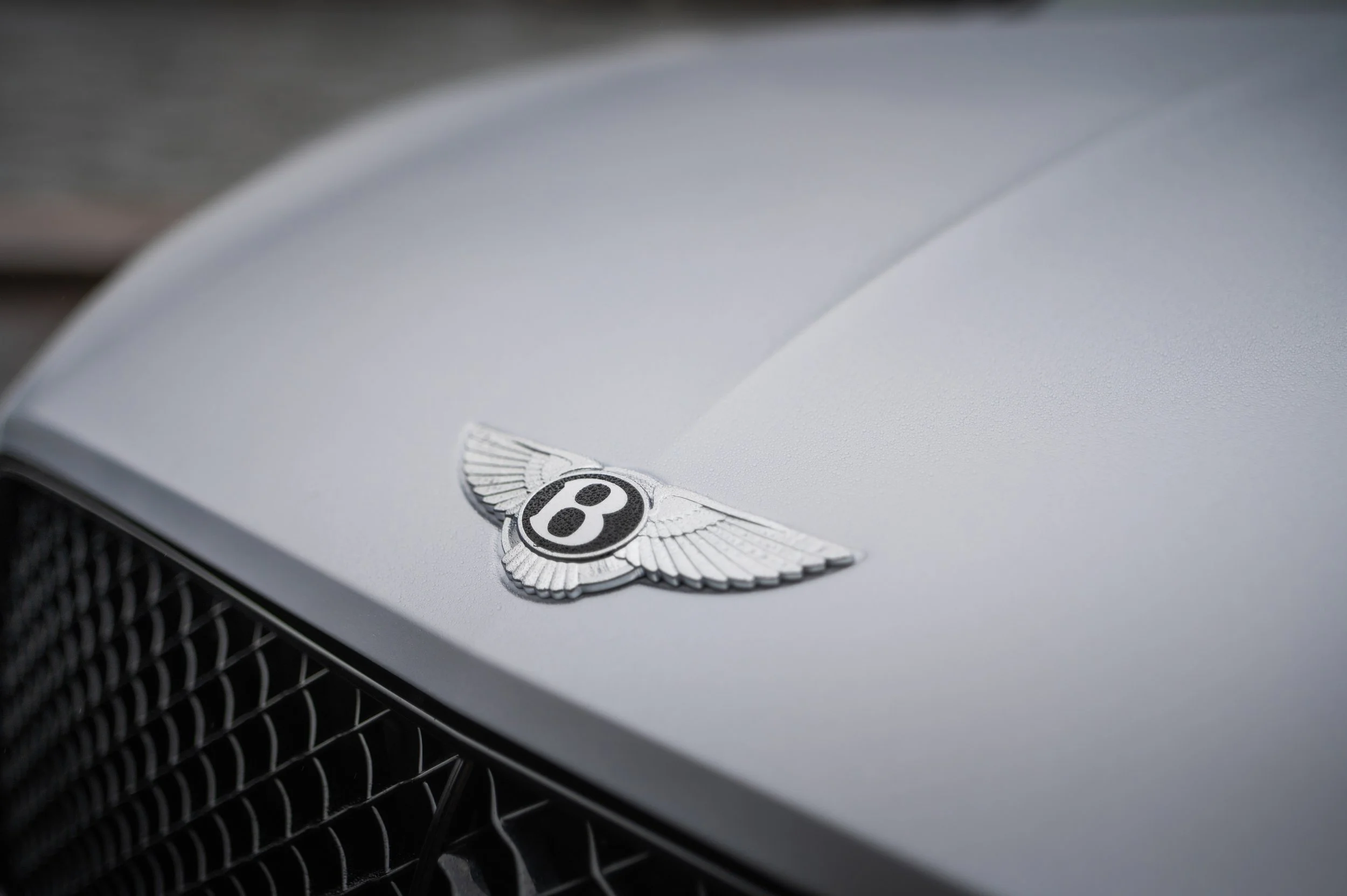 Close-up of a silver Bentley logo on the hood of a car.