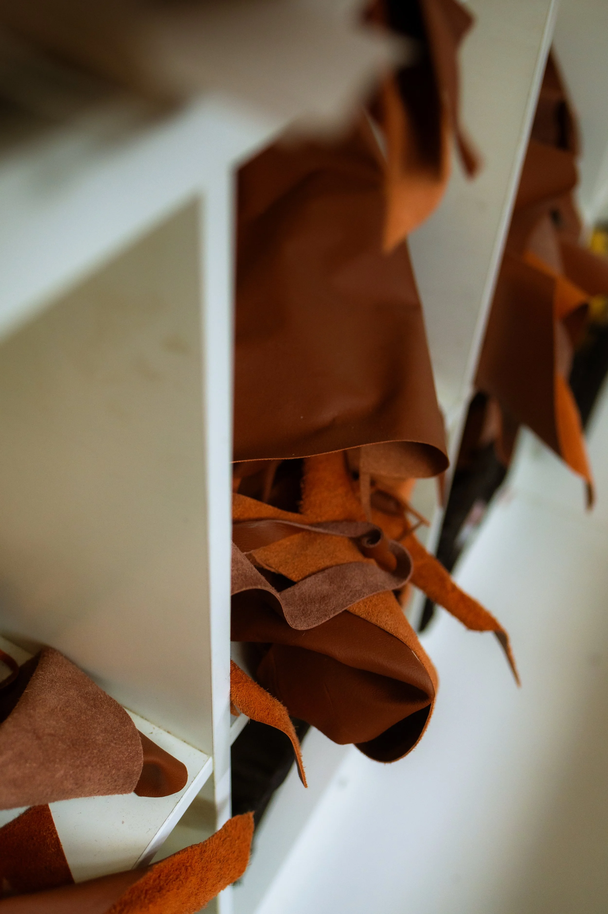 A close-up of various shades of orange and brown leather and suede swatches hanging from a white storage unit.
