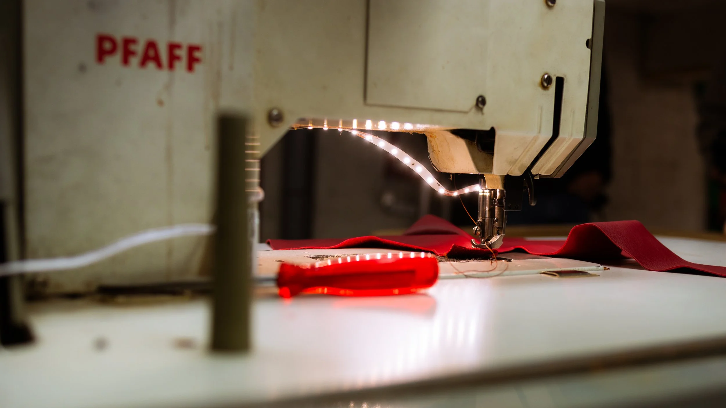 Close-up of a sewing machine stitching red fabric with the brand name PFAFF visible on the machine.