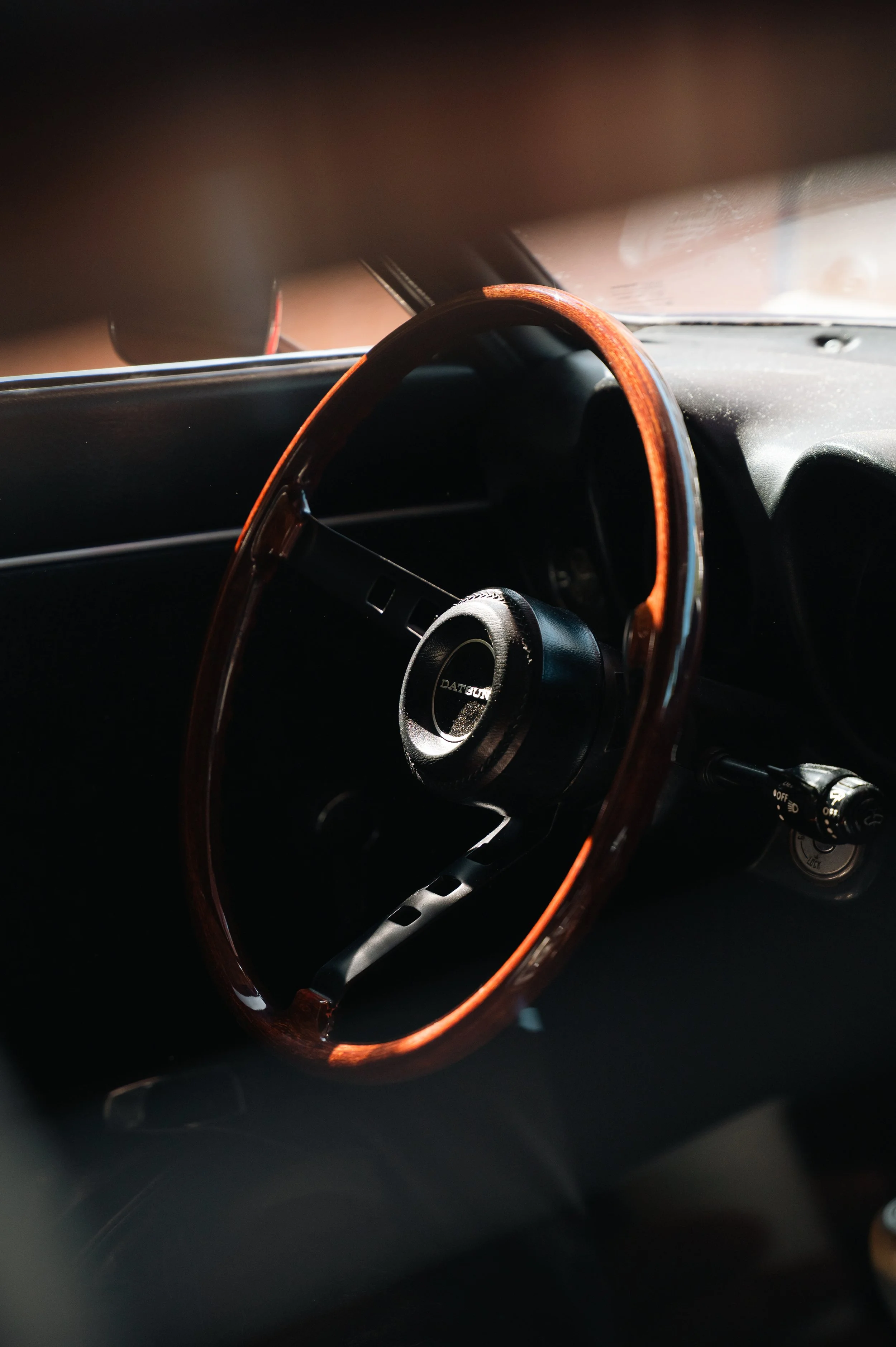 Close-up of a classic car's interior featuring a wooden steering wheel and dashboard, with sunlight casting shadows inside the vehicle.