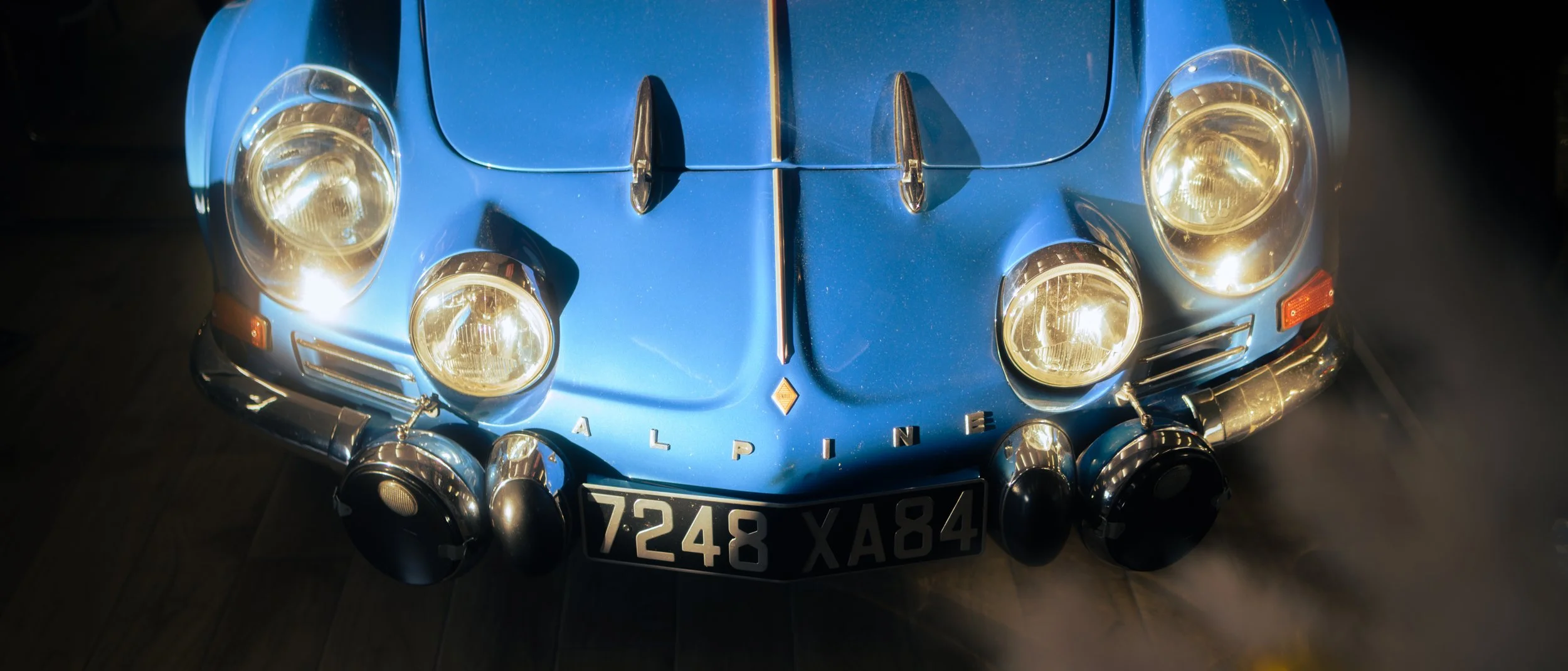 Front view of a vintage blue Alpine sports car with four headlights, a black grille, and a European (French) license plate.