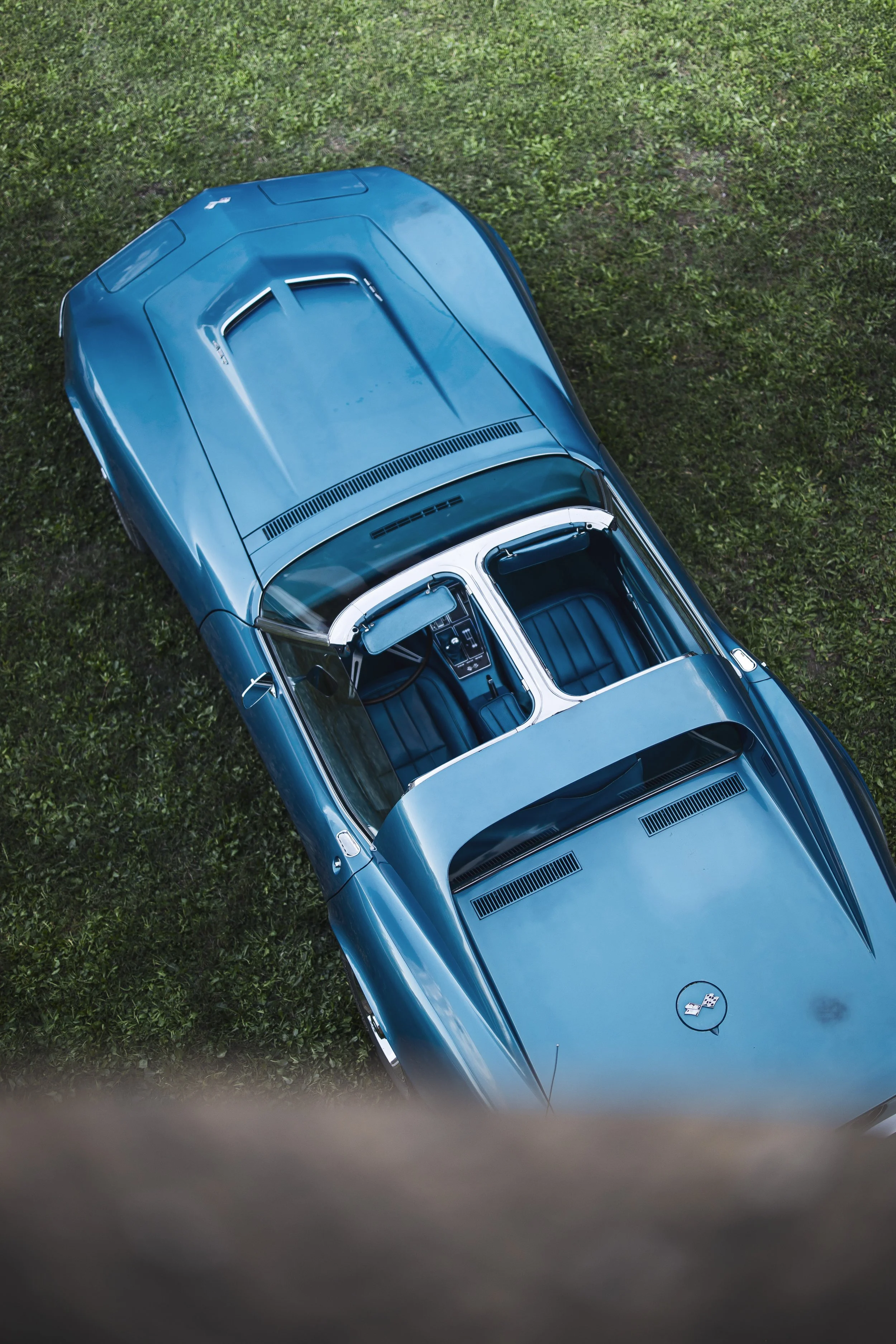 Top-down view of a blue classic Chevrolet Corvette car parked on green grass.