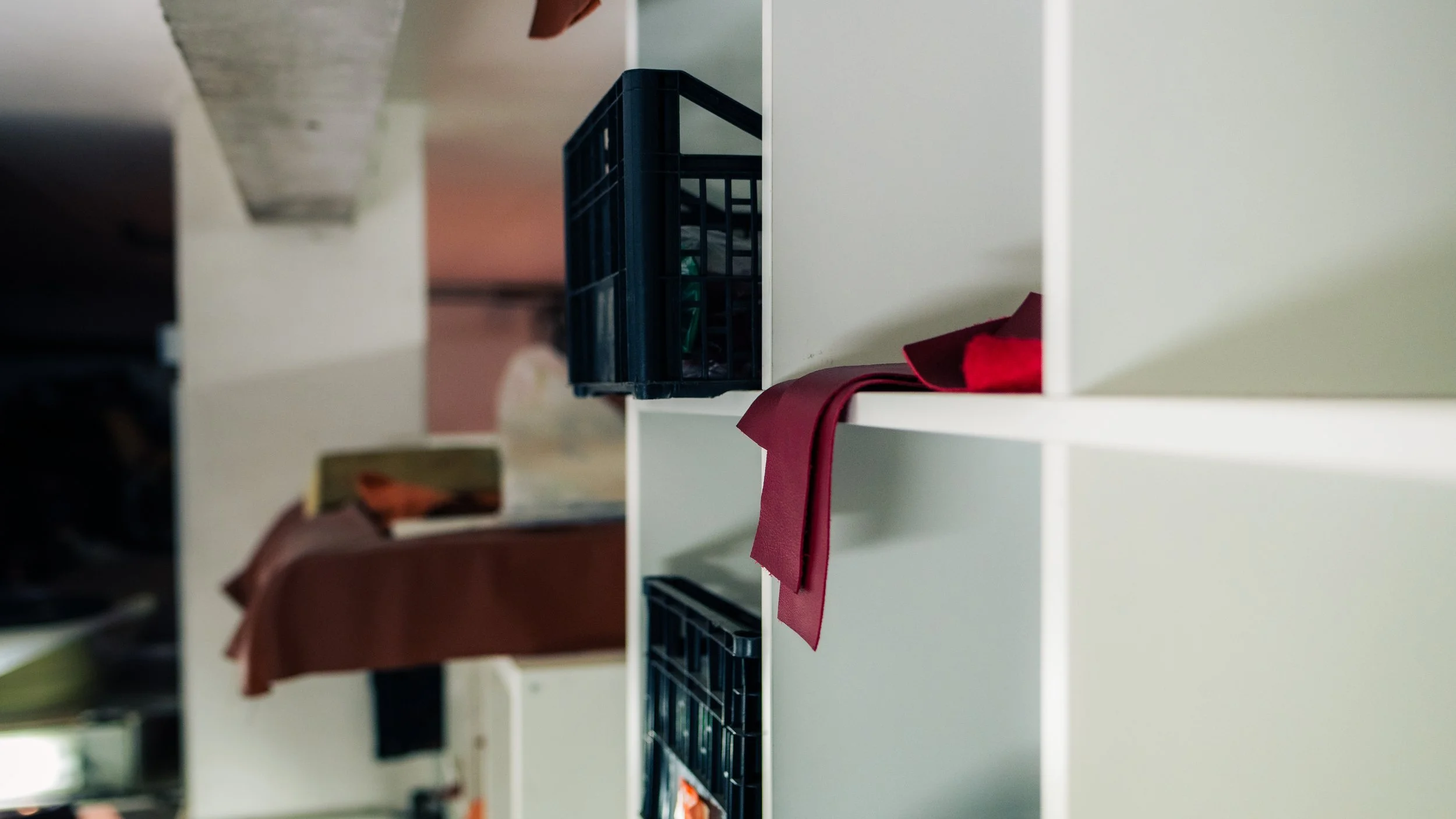 A white shelf with black storage boxes, one with a red cloth draped over it, in a room with a bed and other furniture.