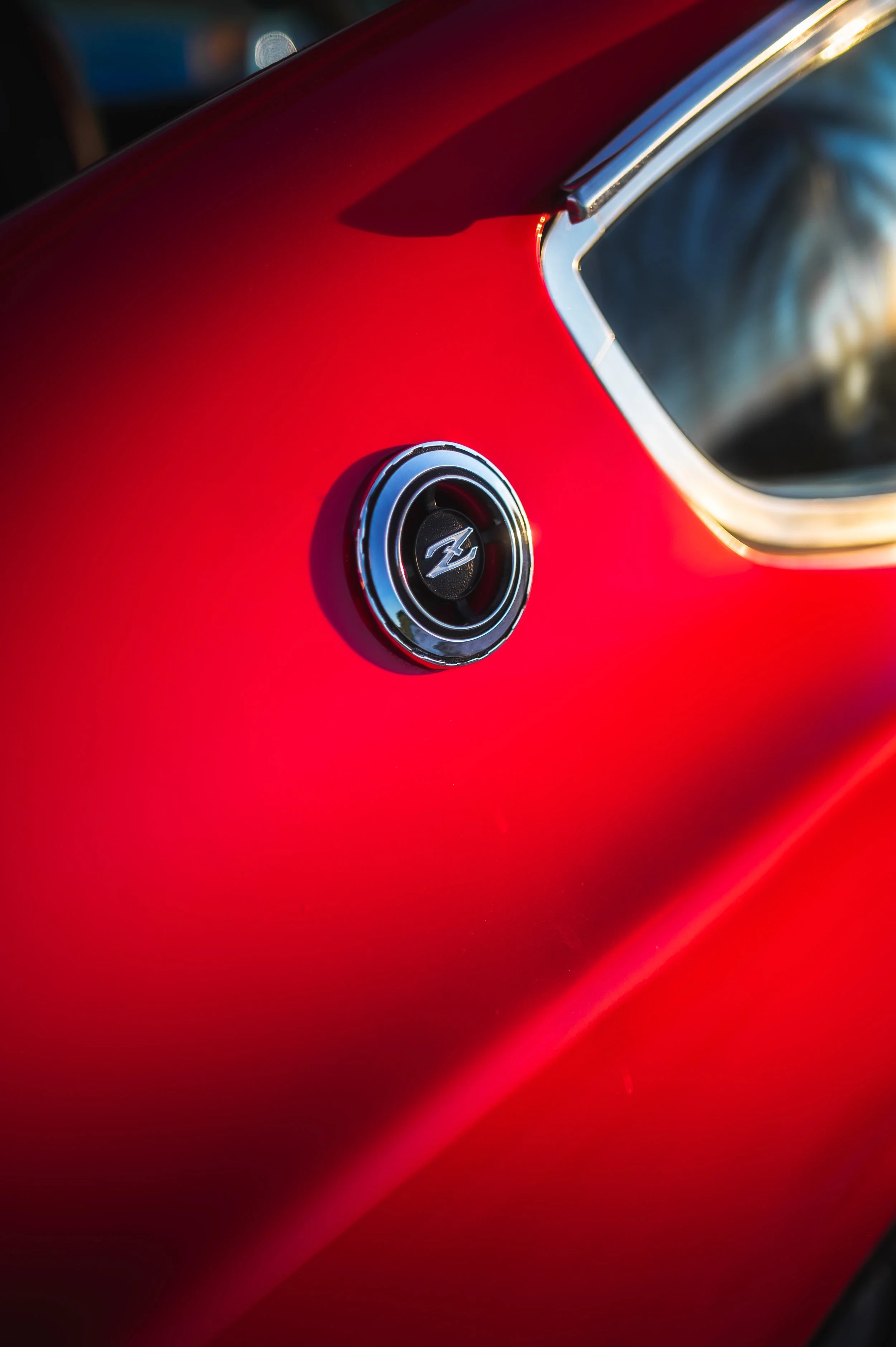 Close-up of a red Datsun 240Z with a round air vent featuring a stylized logo near the rear window.