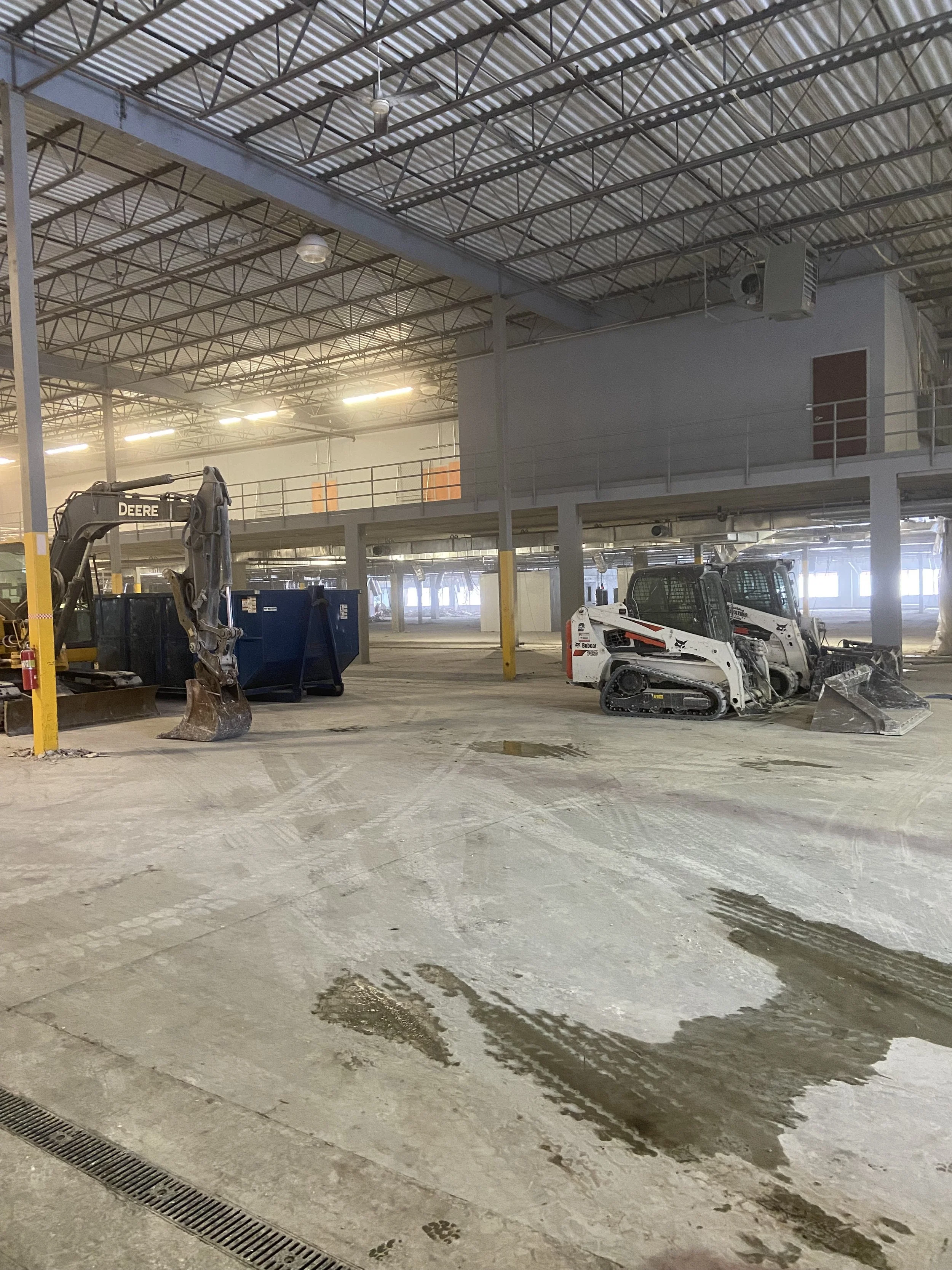 Empty indoor commercial demolition construction site with two small skid-steer loaders and construction debris