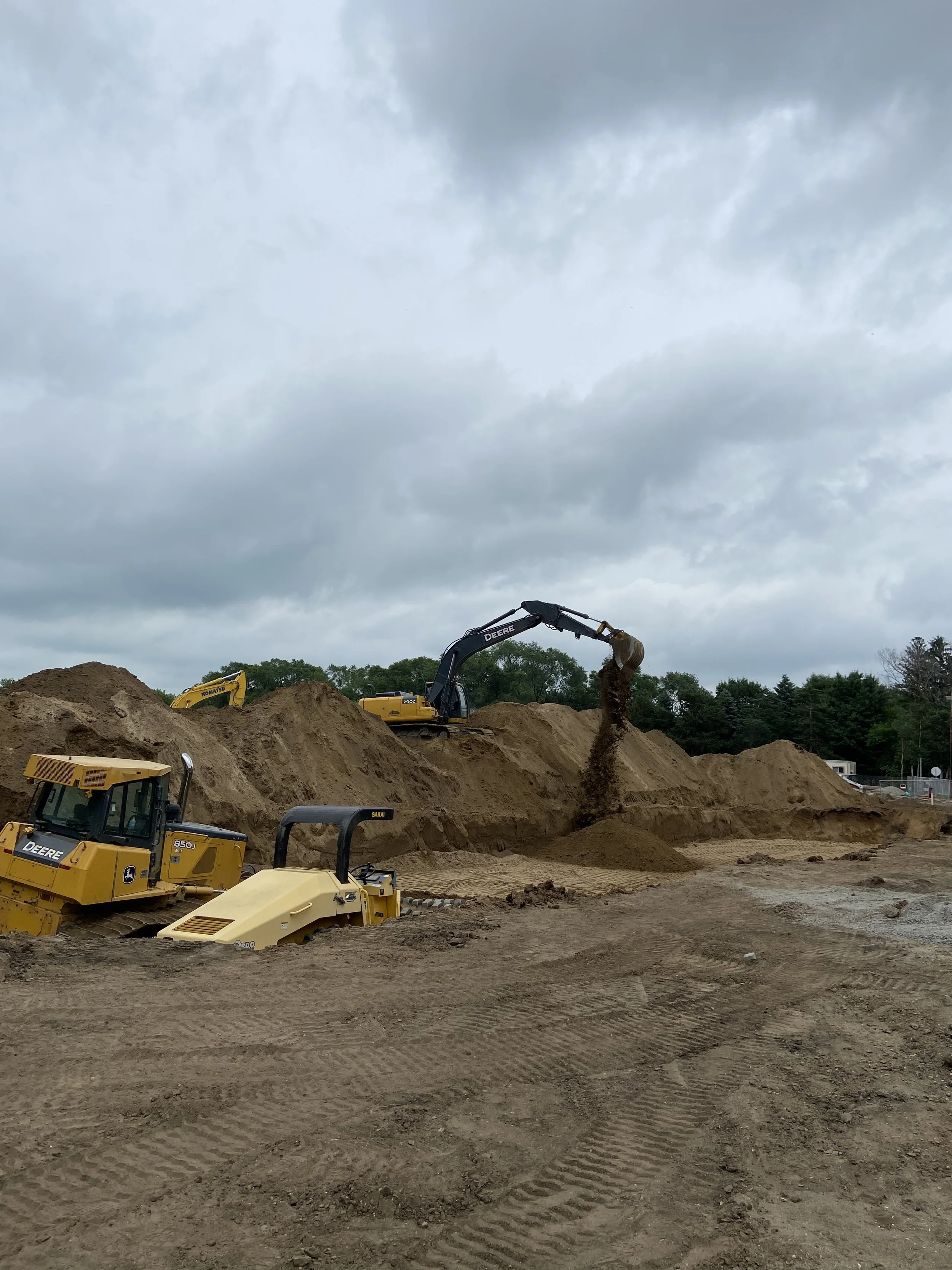 Construction site with yellow and black excavators digging and moving dirt on a cloudy day.