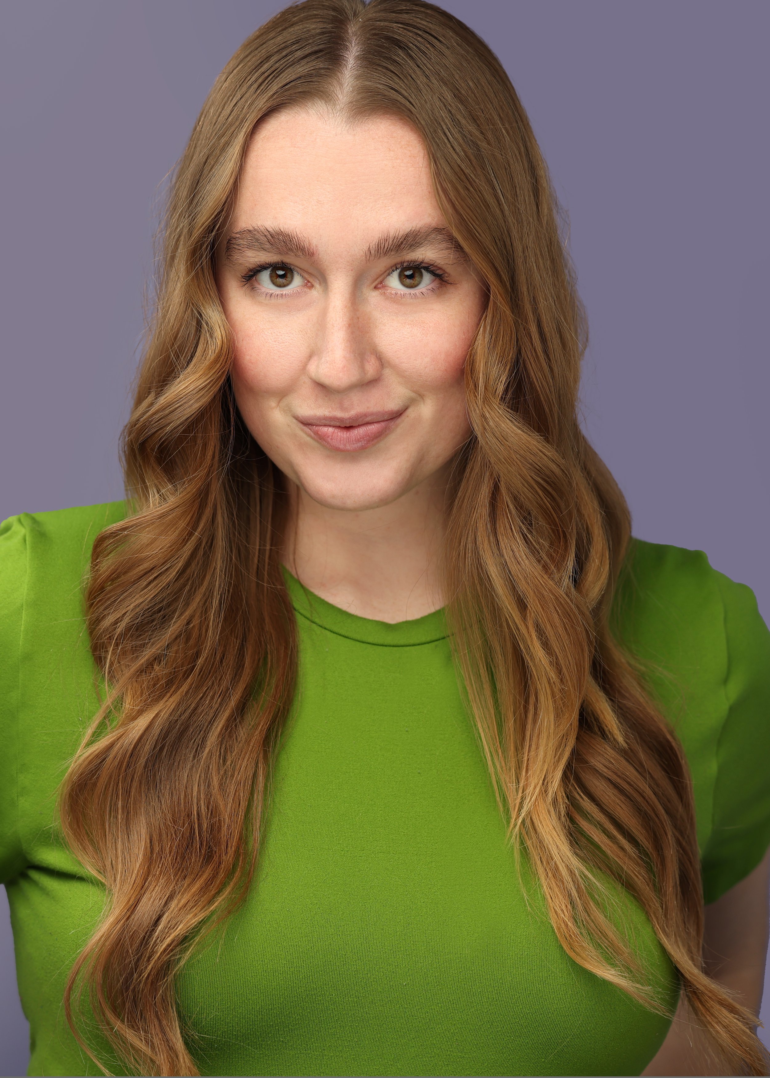 A woman with long wavy red hair, wearing a bright green top, smiling, against a purple background.