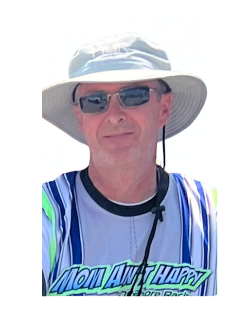 Man wearing a wide-brimmed hat, sunglasses, and a striped shirt, smiling outdoors.