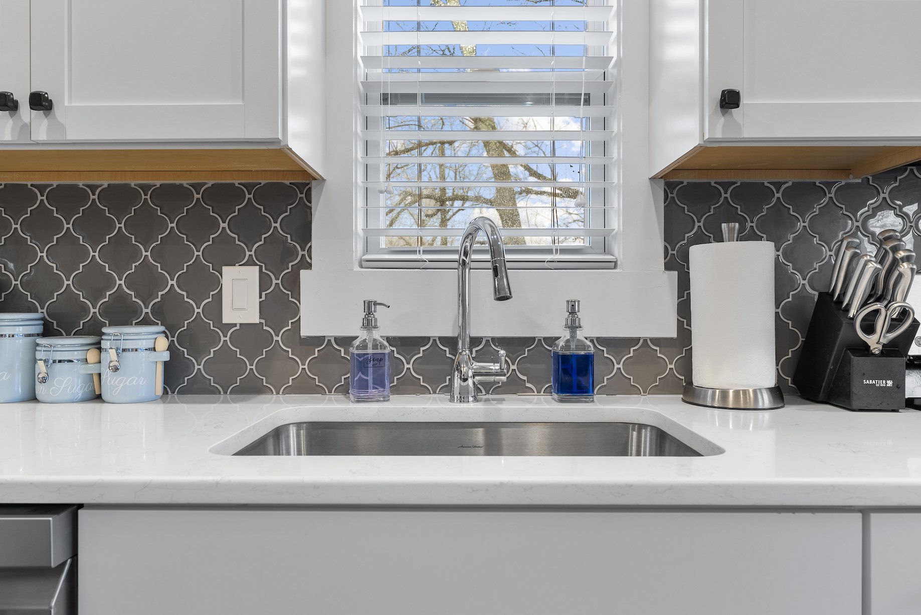 Clean kitchen sink area with white countertops, classic tile backsplash, and natural light in a charming Ball Ground, GA short-term rental.