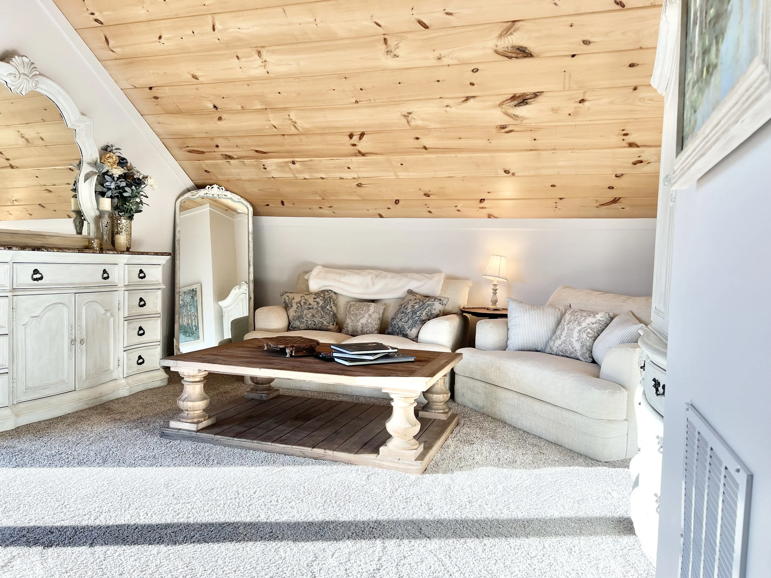 	
Inviting sitting area in primary bedroom with a wood coffee table, comfortable seating, and wall-mounted TV in a warm French country–inspired Ball Ground, GA short-term rental.