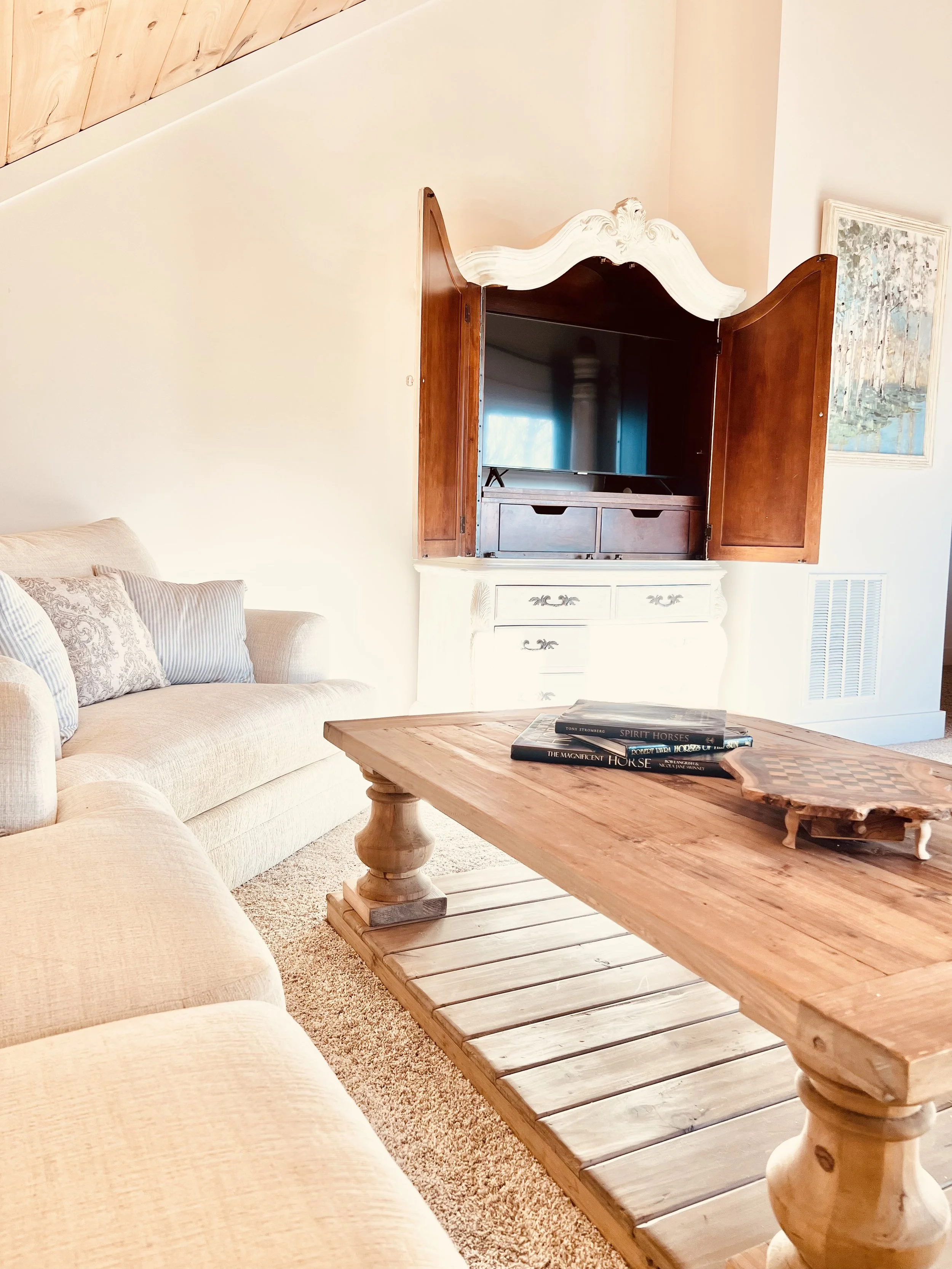 Inviting sitting area in primary bedroom with a wood coffee table, comfortable seating, and wall-mounted TV in a warm French country–inspired Ball Ground, GA short-term rental.
