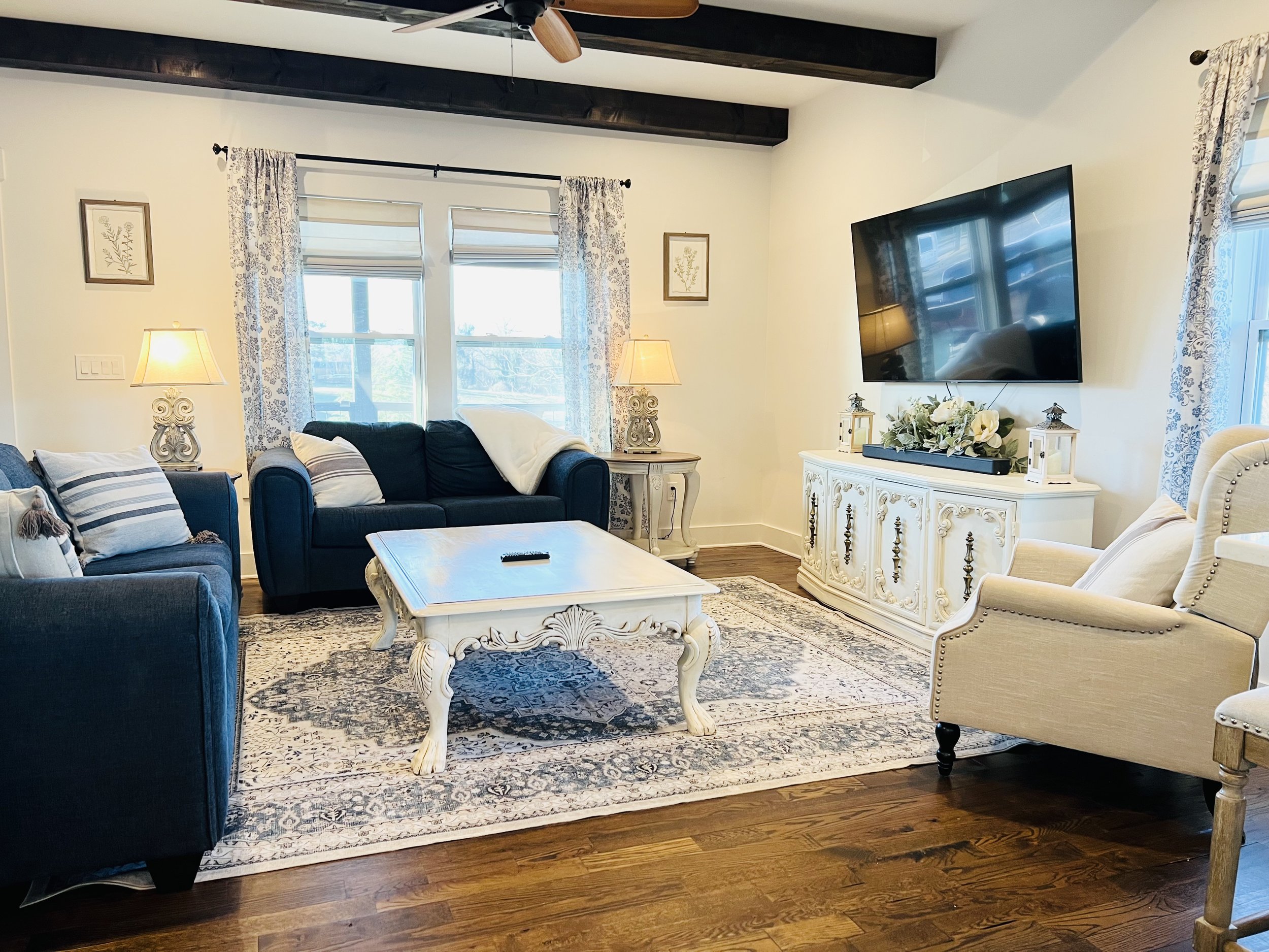 Open-concept living room with French country decor, navy and white seating, elegant sideboard, and large windows, connecting to the kitchen at a Ball Ground, Georgia vacation rental
