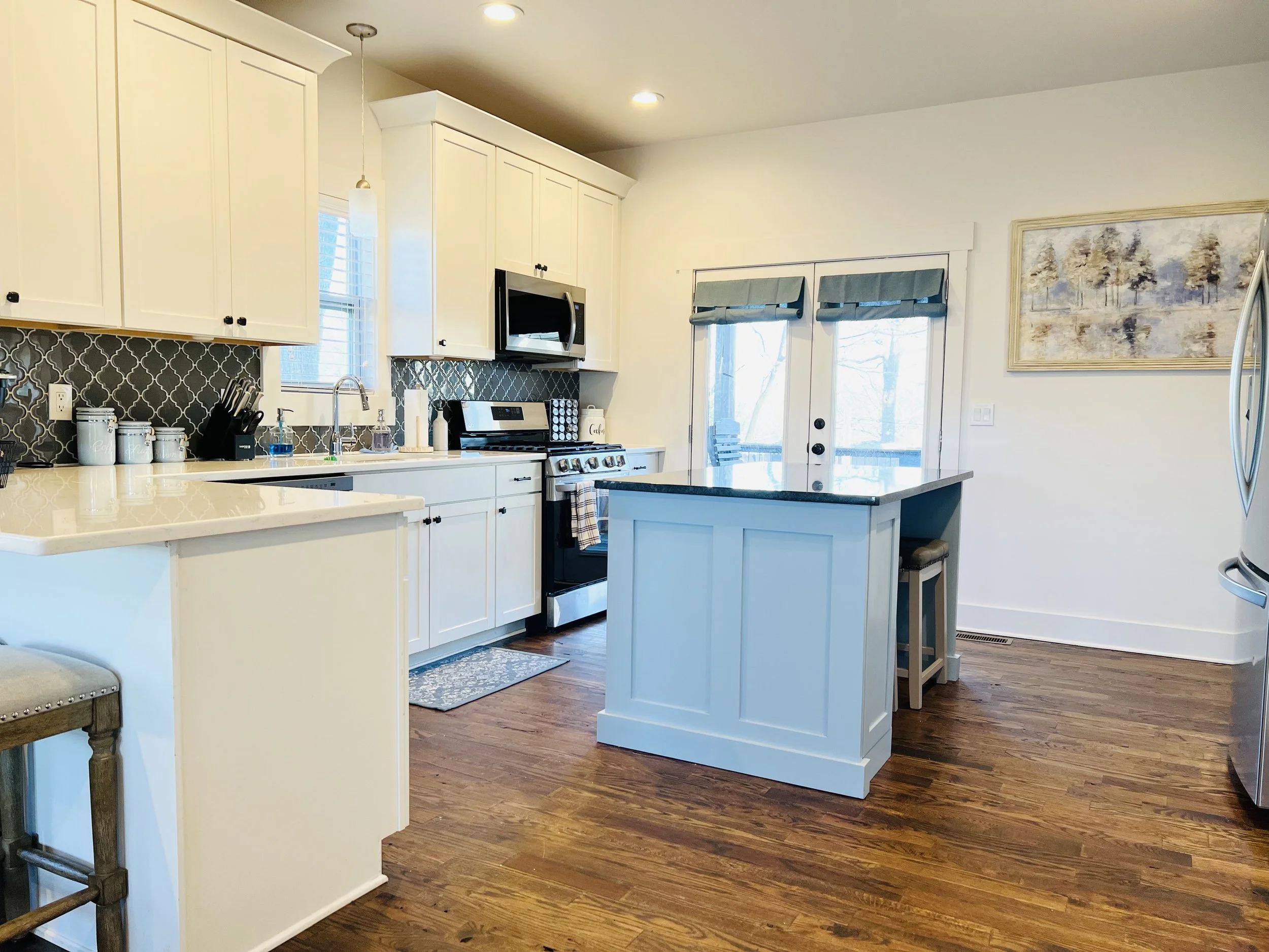 Bright, open kitchen with white cabinetry, a center island, hardwood floors, and bar seating at a Ball Ground, Georgia vacation rental.