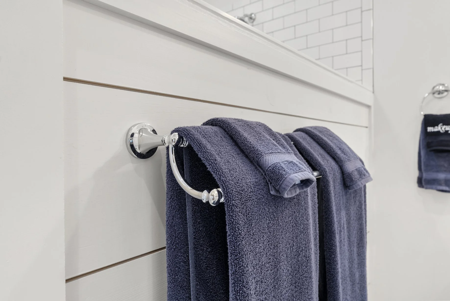 A dark blue towel hanging on a chrome towel ring attached to a white bathroom wall, with a second towel or washcloth folded on top of it at Ball Ground Vacation Rental. 
