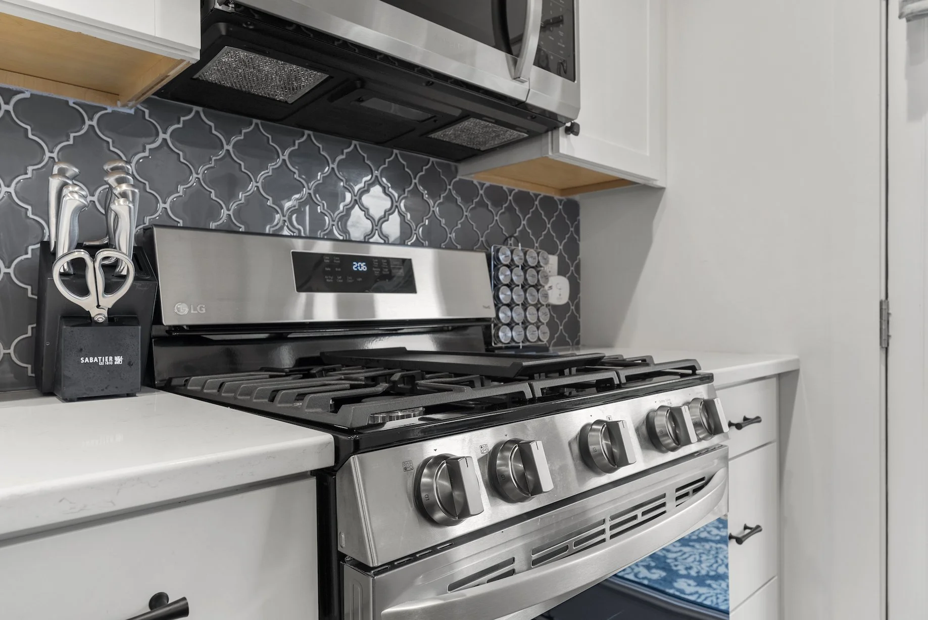 Modern kitchen with a stainless steel gas range, tile backsplash, and white cabinetry at a Ball Ground, Georgia vacation rental.