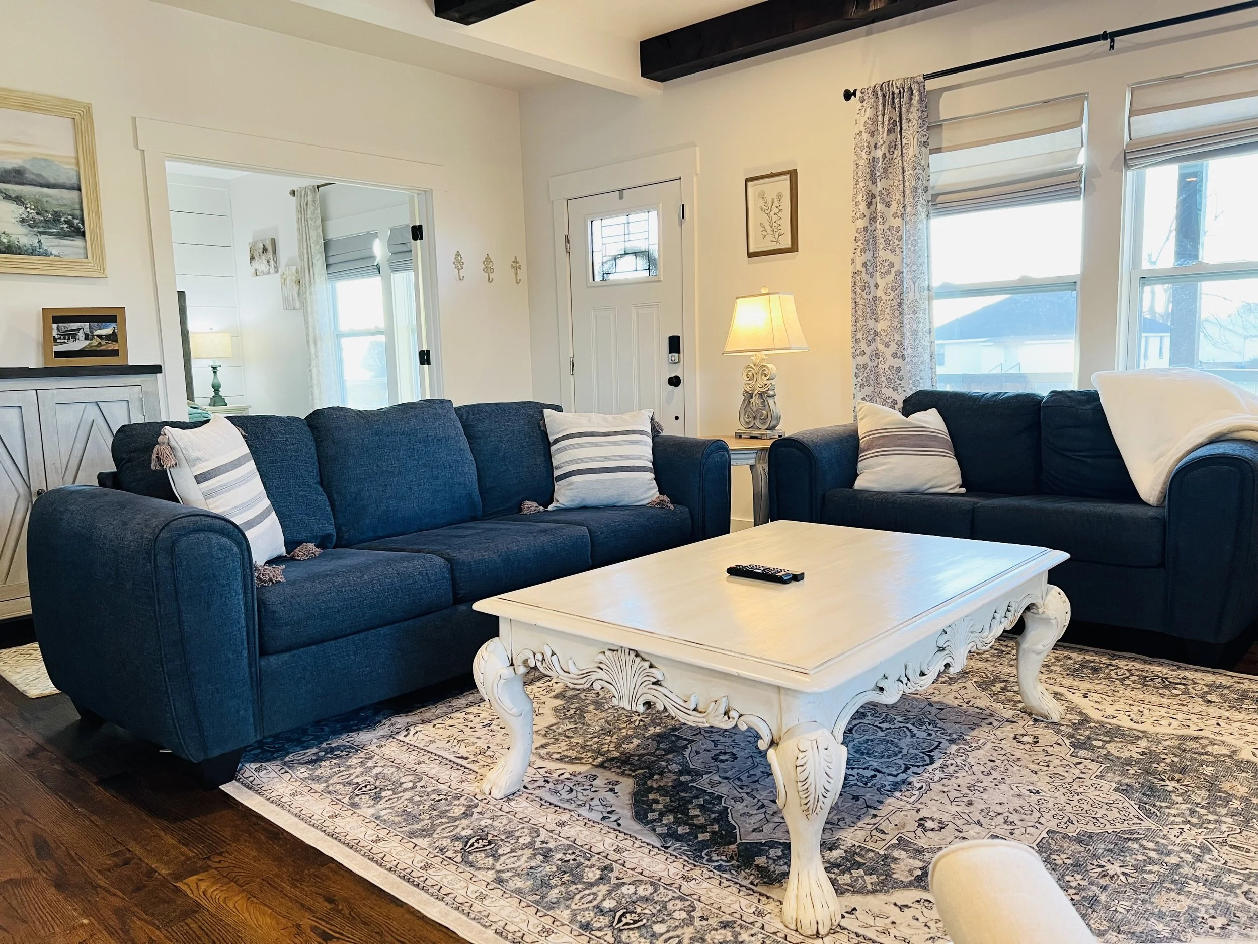Open-concept living room with French country decor, navy and white seating, elegant sideboard, and large windows, connecting to the kitchen at a Ball Ground, Georgia vacation rental