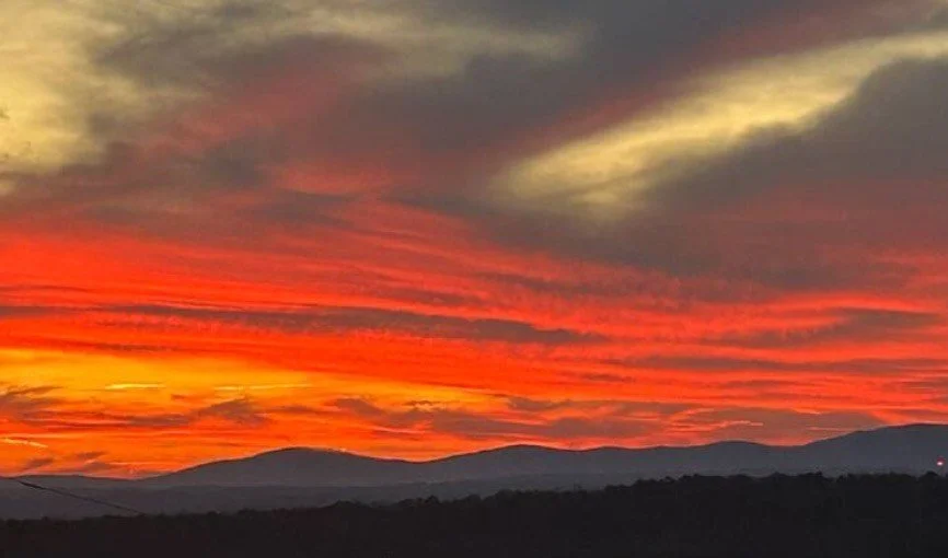 A vibrant sunset over mountain silhouettes with colorful orange, red, and yellow clouds in the sky.