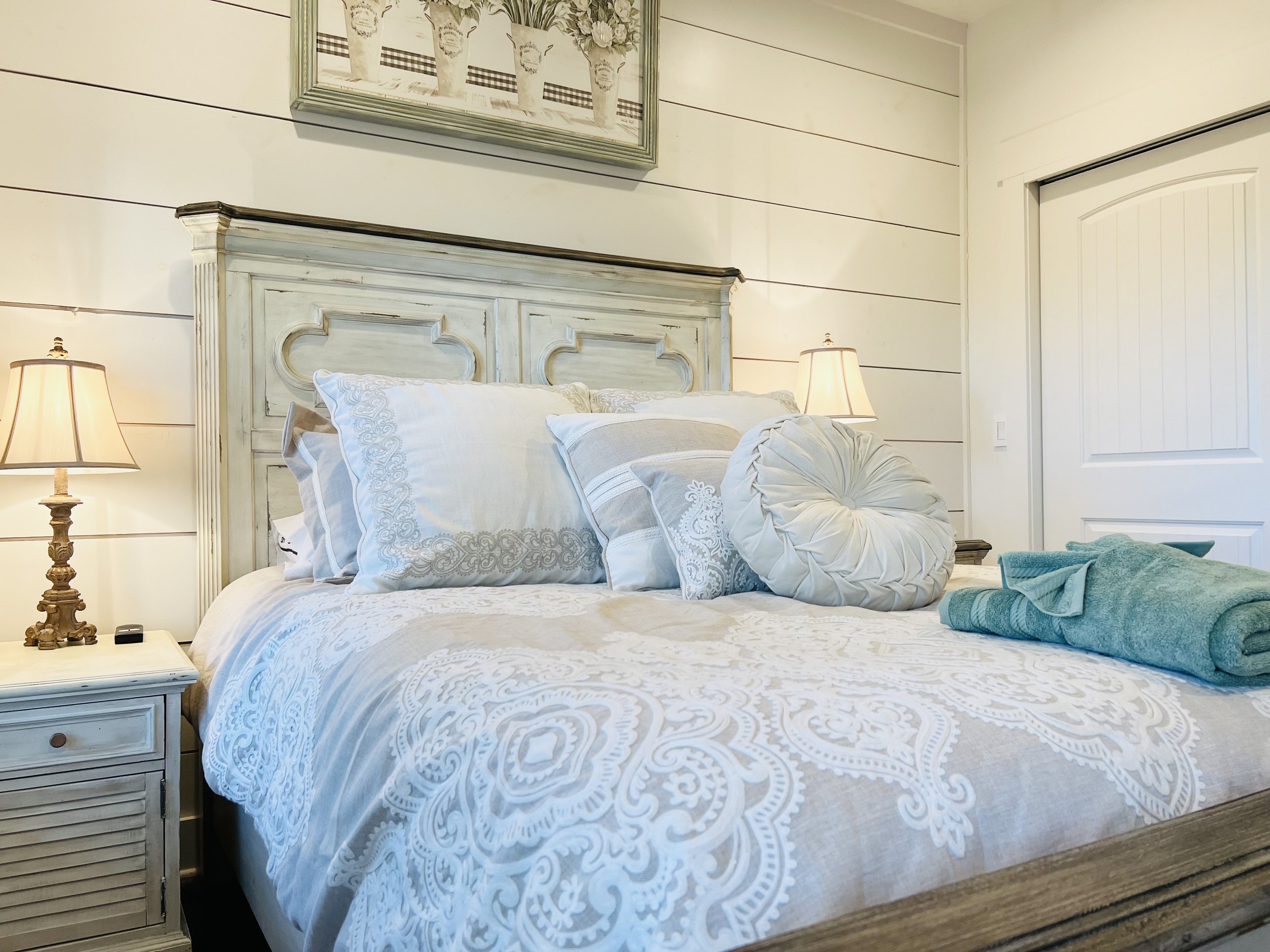 Cozy queen bedroom with a white vintage-style bed, neutral bedding, floral accents, and French country charm in a Ball Ground, GA short-term rental.