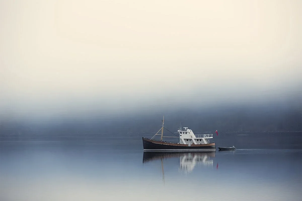 A solitary boat floating on calm, reflective water with a foggy, blurred background.