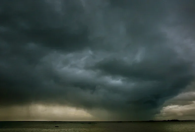 Dark storm clouds over the ocean with rain falling in the distance.