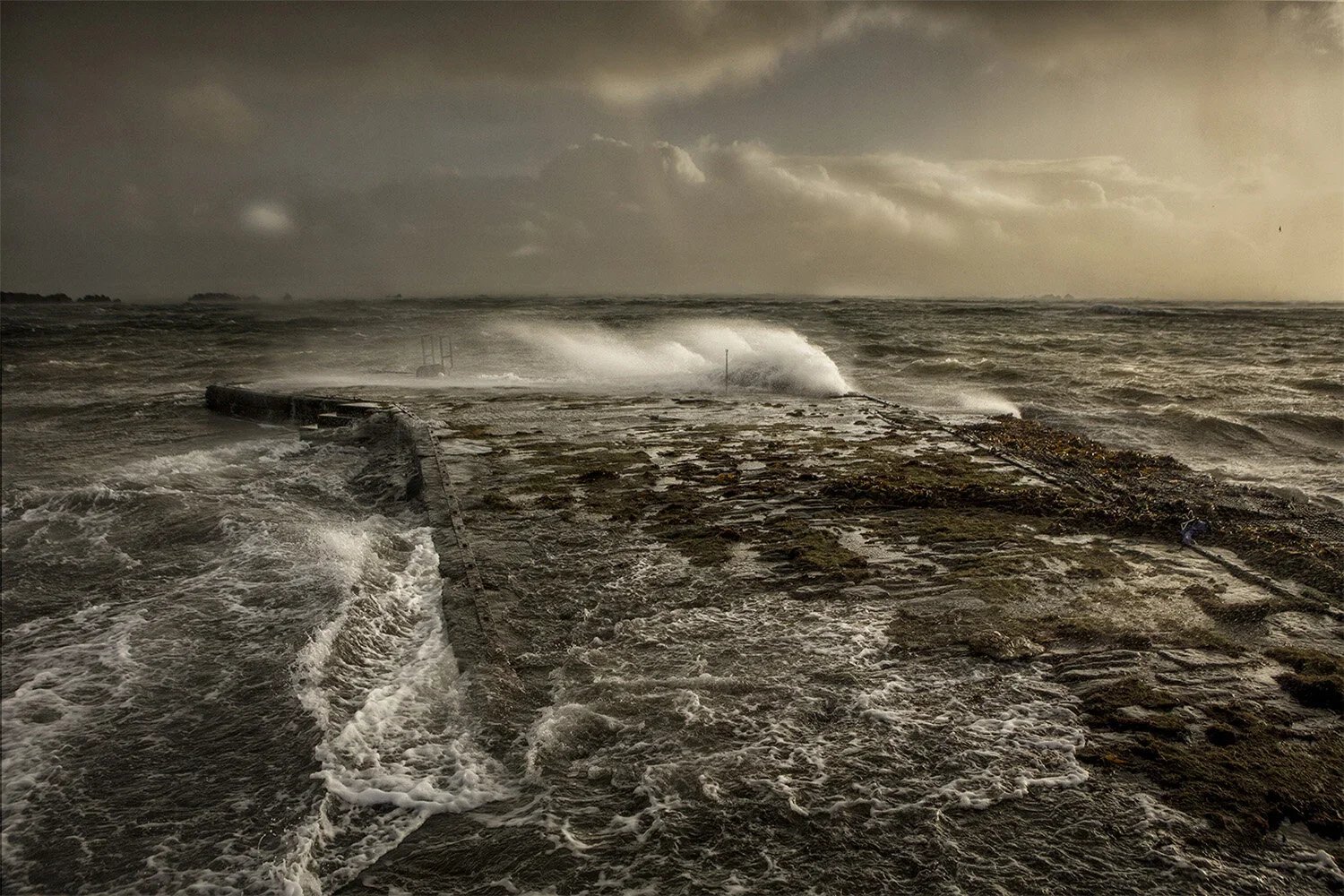 Stormy sea with waves crashing over a concrete pier or breakwater