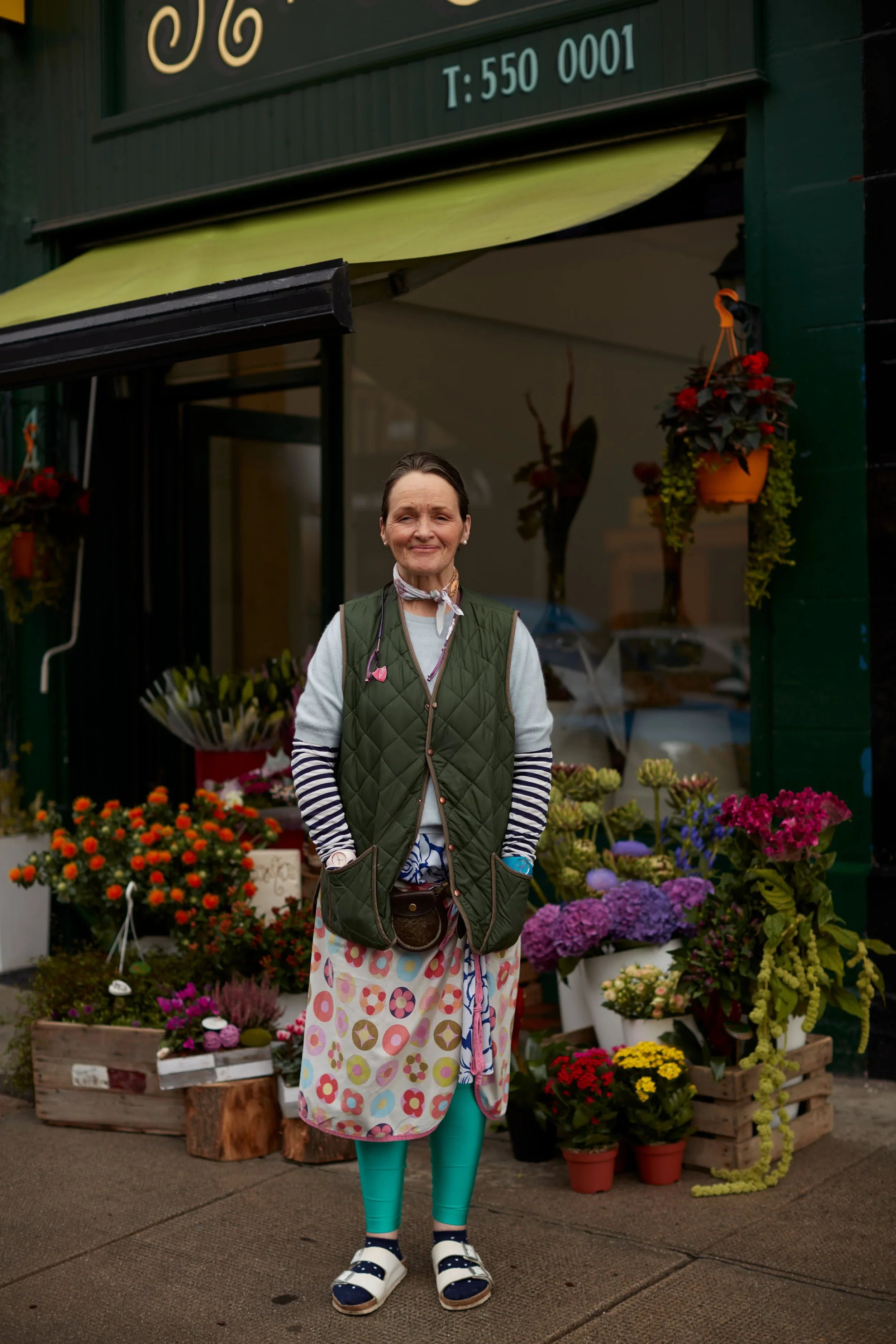 Woman standing outside a flower shop in front of colorful plants and flowers.