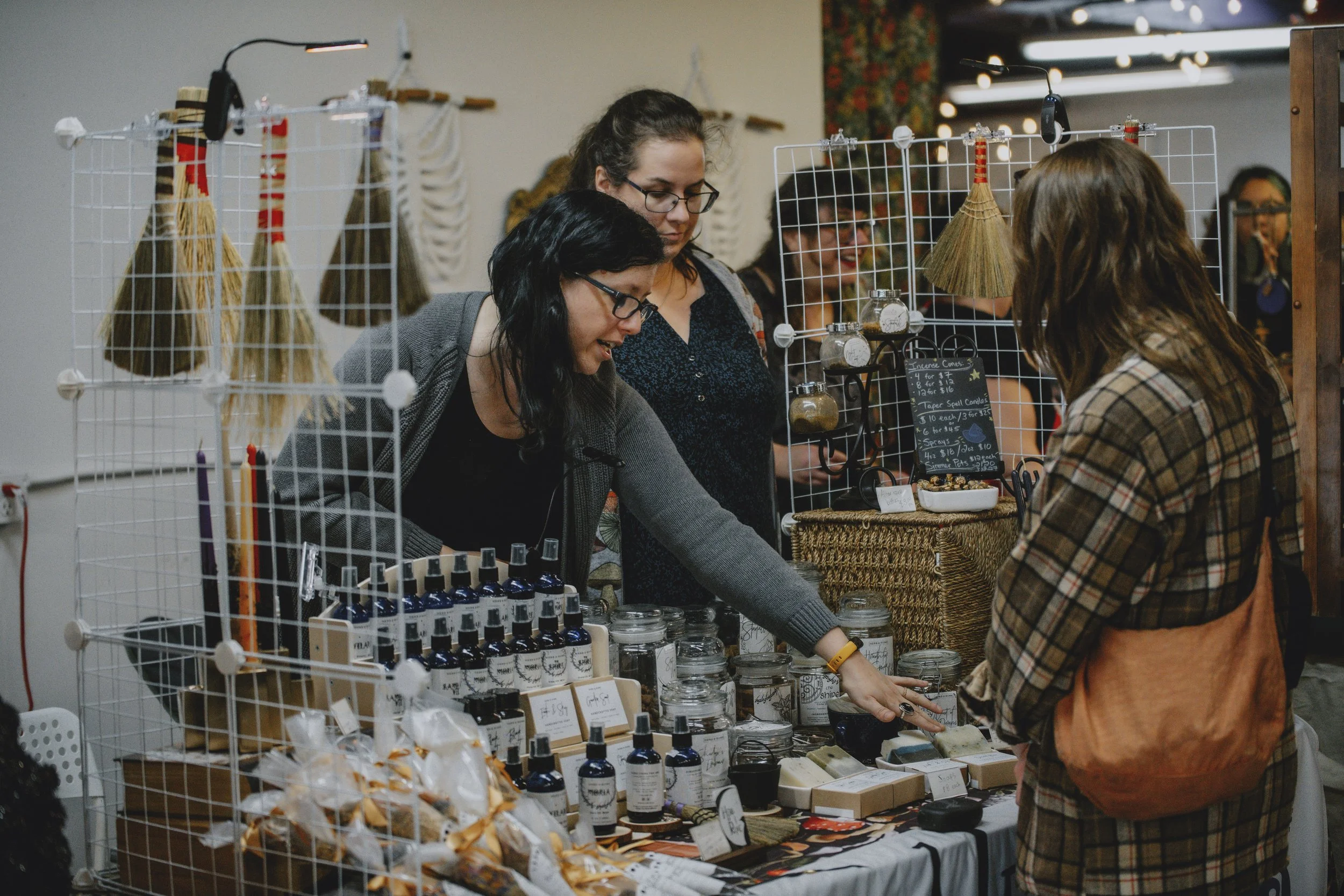 People shopping at a market stall with handmade soap, bottles of essential oil, and natural products.