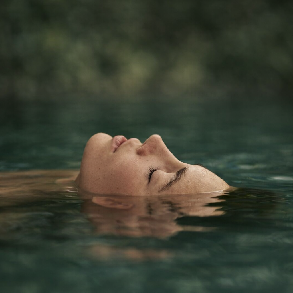 Close-up of a woman floating peacefully on her back in a body of water with her eyes closed.