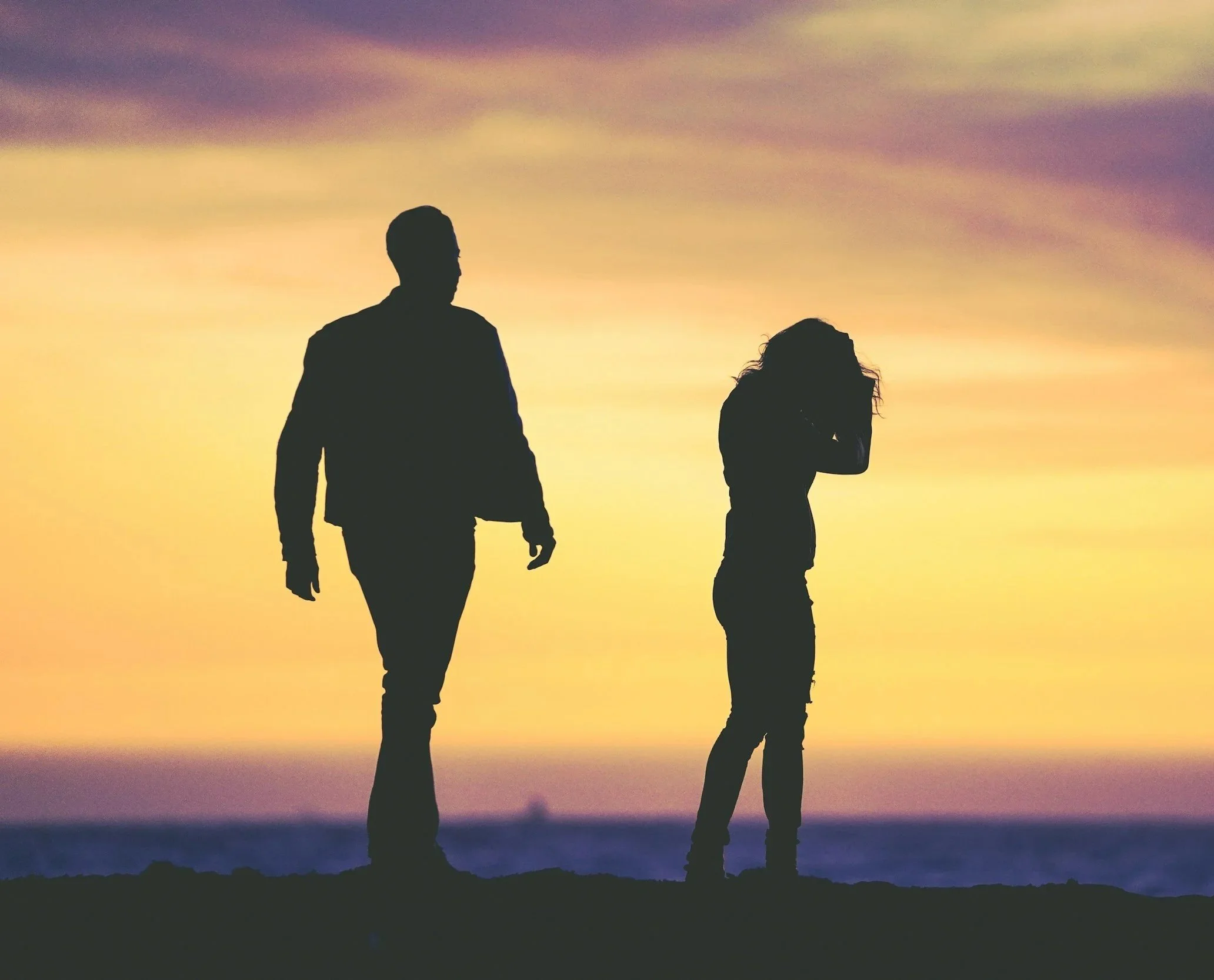 Silhouettes of a man and a woman walking outdoors during sunset, with colorful sky in the background.