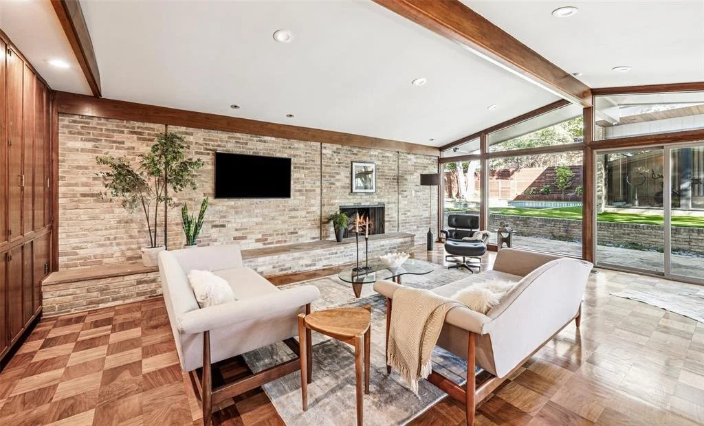 True authentic Mid-Century Modern Architecture with bright living room, large windows, brick wall fireplace, white sofas, glass coffee table, and wooden accents in Janmar neighbrhood of North Dallas, Texas.