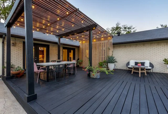 Outdoor patio deck with string lights, a dining table with pink and black chairs, and a seating area with a sofa, coffee table and succulents in Brookhaven Club, Farmers Branch, TX.