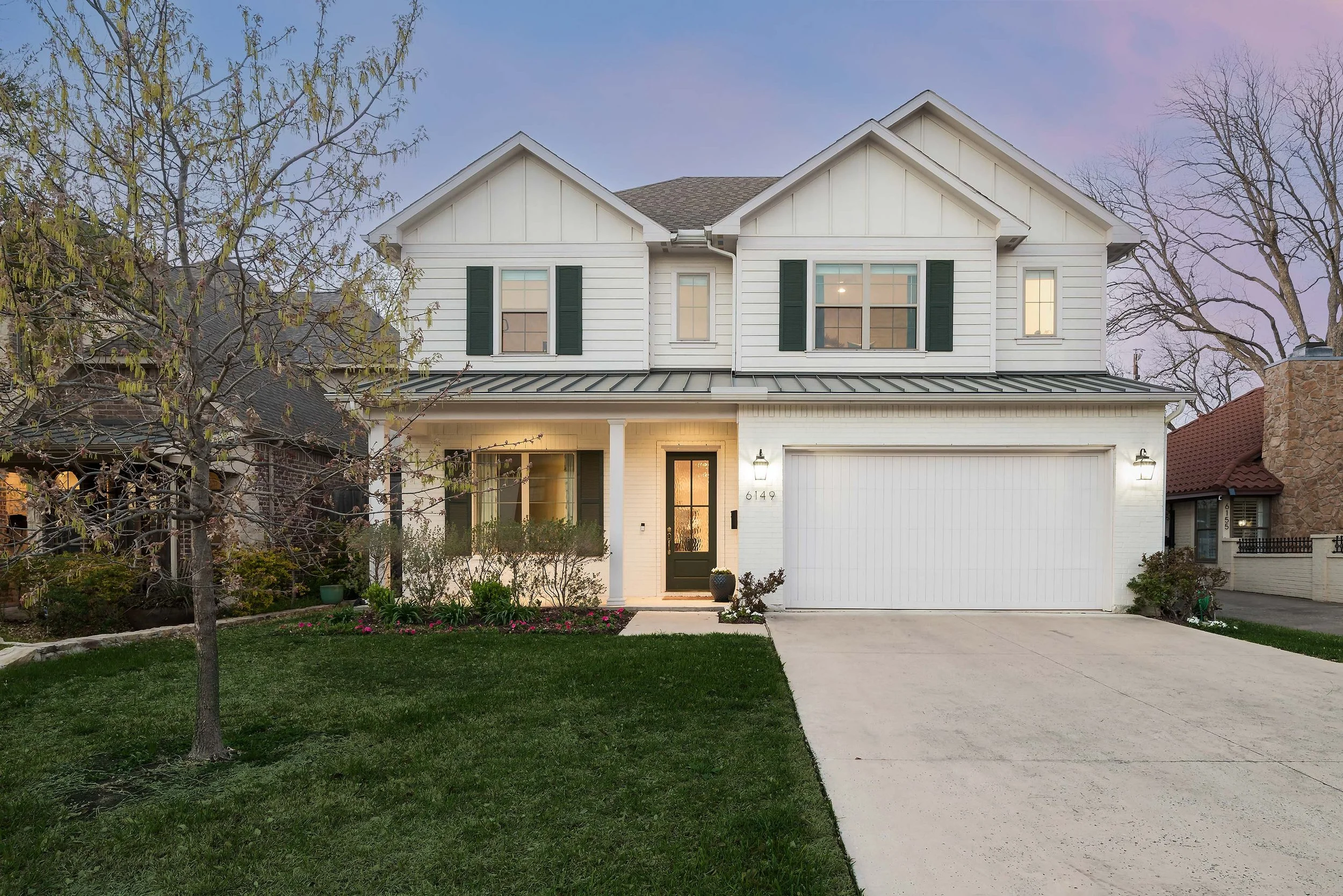 White two-story transitional farmhouse style architecture with dark green shutters, front door, and a double garage, surrounded by a green lawn and trees in the Lakewood Heights neighborhood of Dallas, TX.