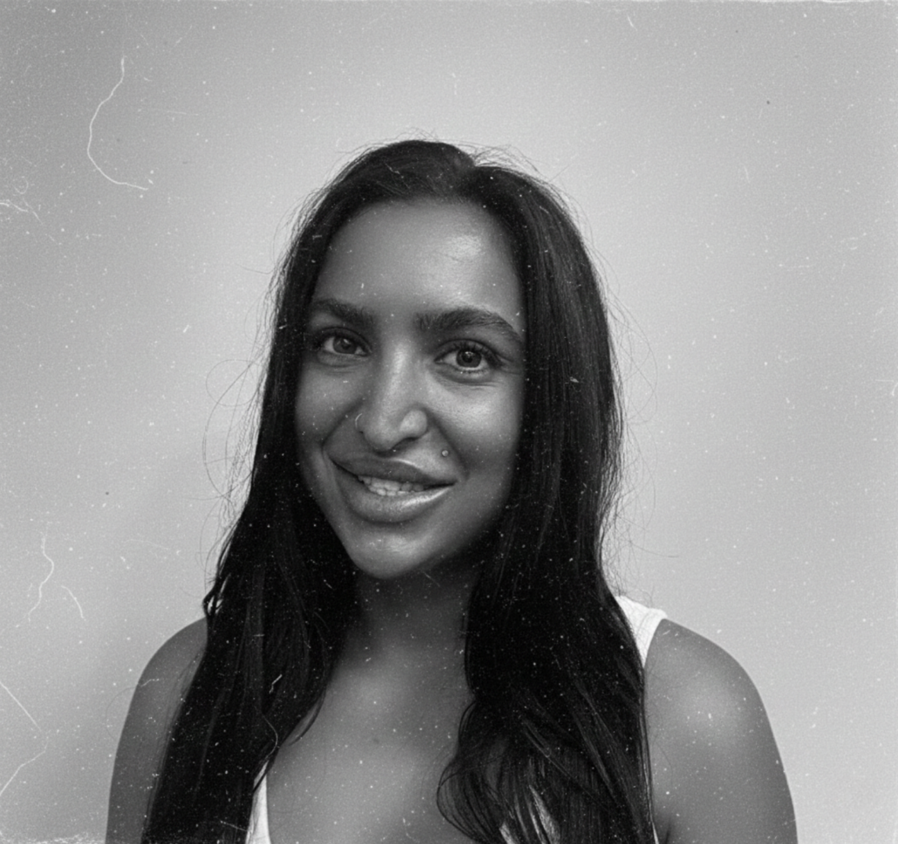 A black and white portrait of a woman with long dark hair, smiling and looking at the camera, against a plain background.