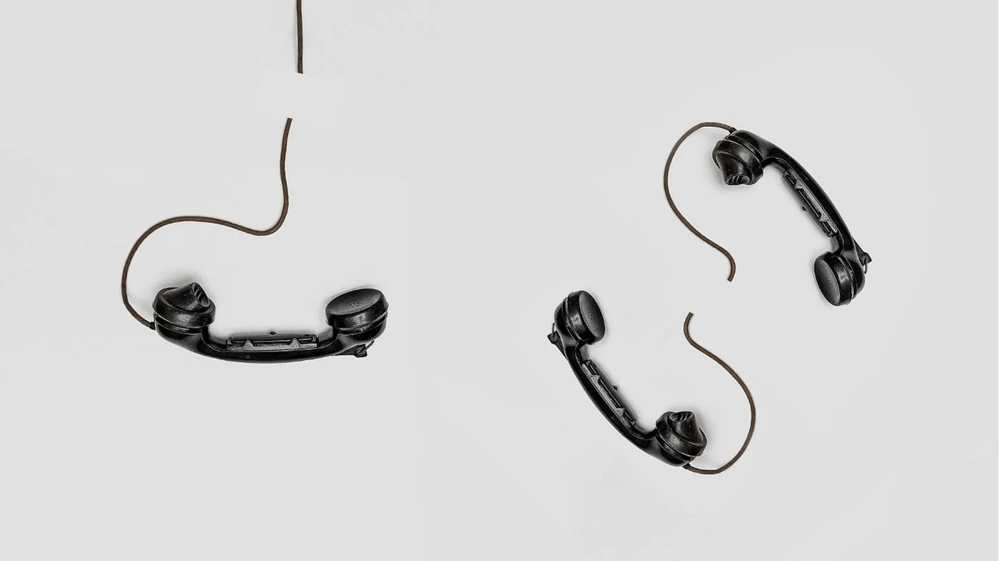 Two landline telephones with torn cords laying on a flat white surface.