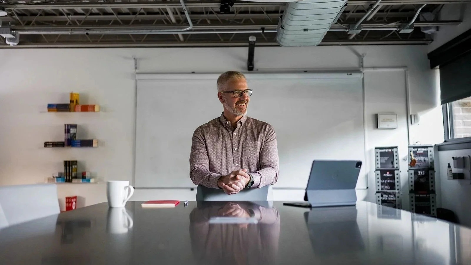 Man smiling with a whiteboard behind him and laptop on his desk, teaching people how to reduce owner dependency