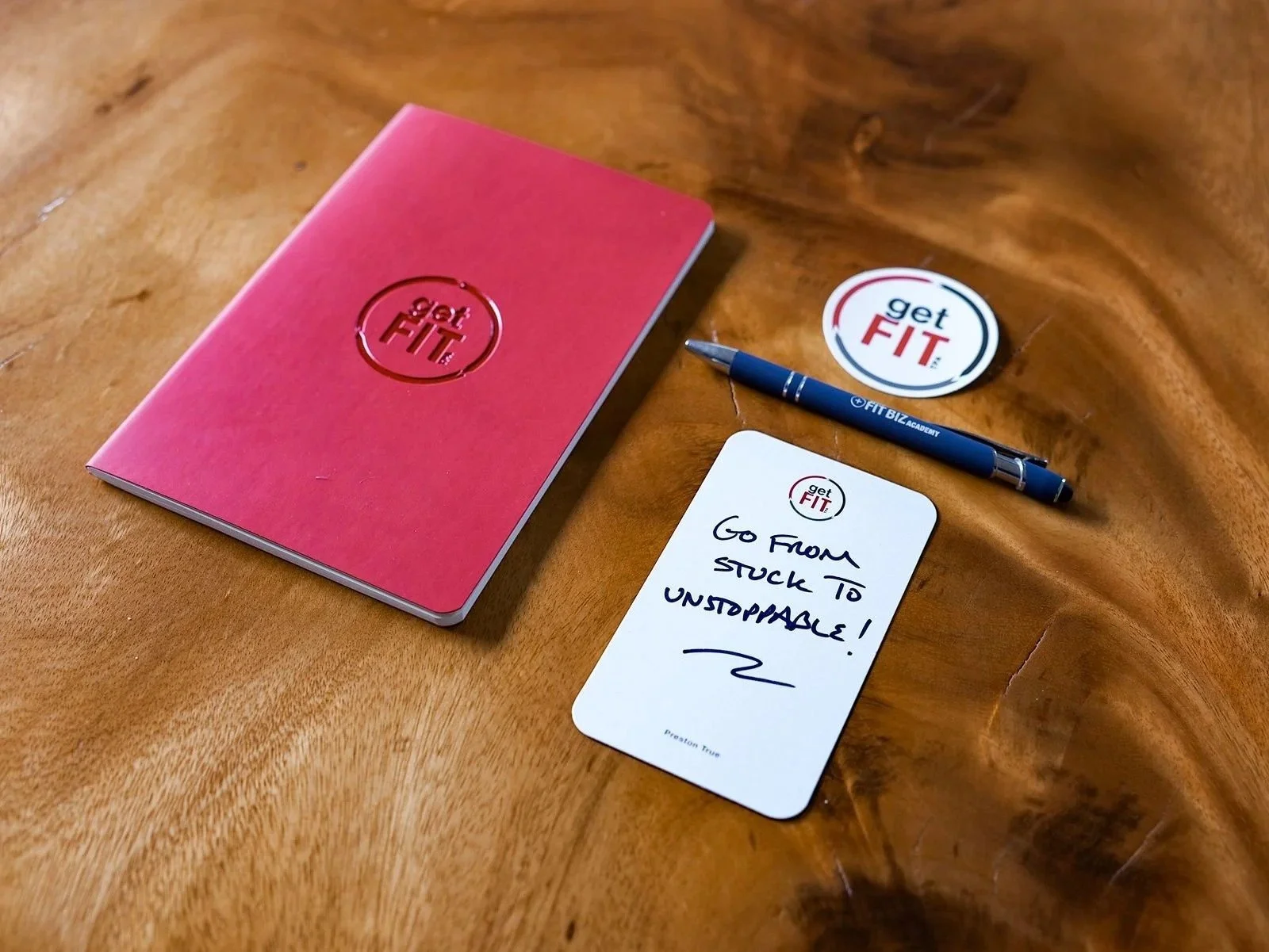A red "Get Fit TPA" journal, sticker, and notepad, a company that helps business owners reduce owner dependency.