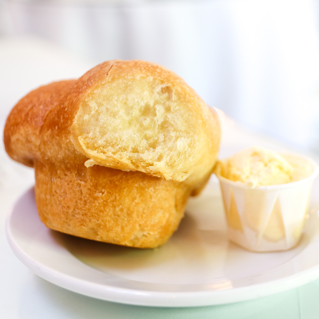 Close-up of a golden fried bread roll with a bite taken out, served on a white plate with a small cup of butter.