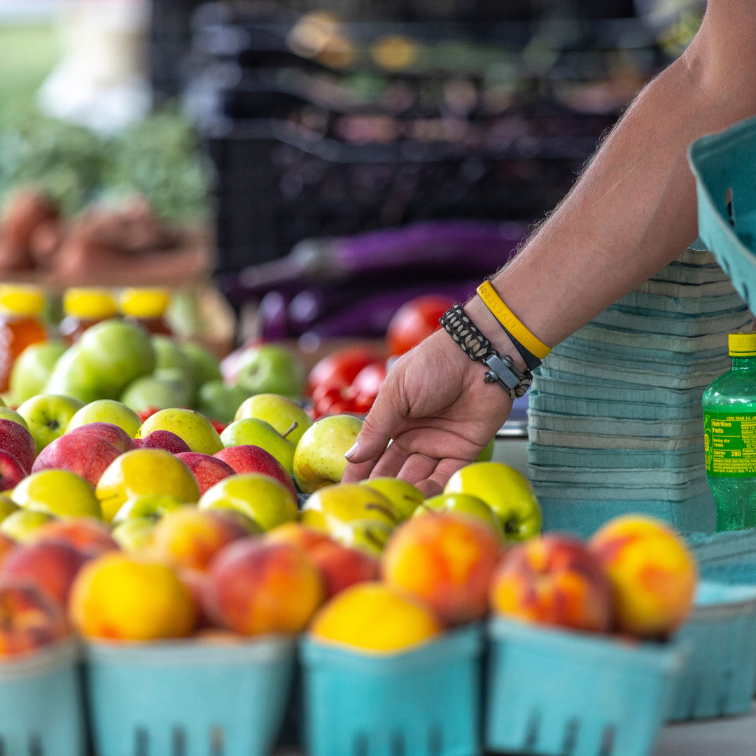 A person shopping at an outdoor market, selecting apples from a display of fresh produce.