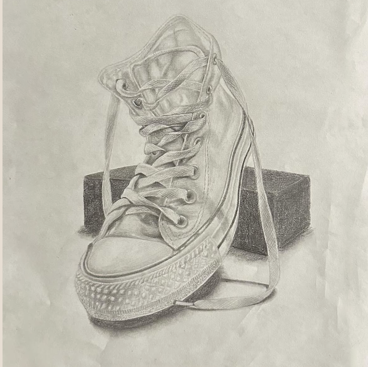 A detailed pencil sketch of a sneaker placed on a small box.