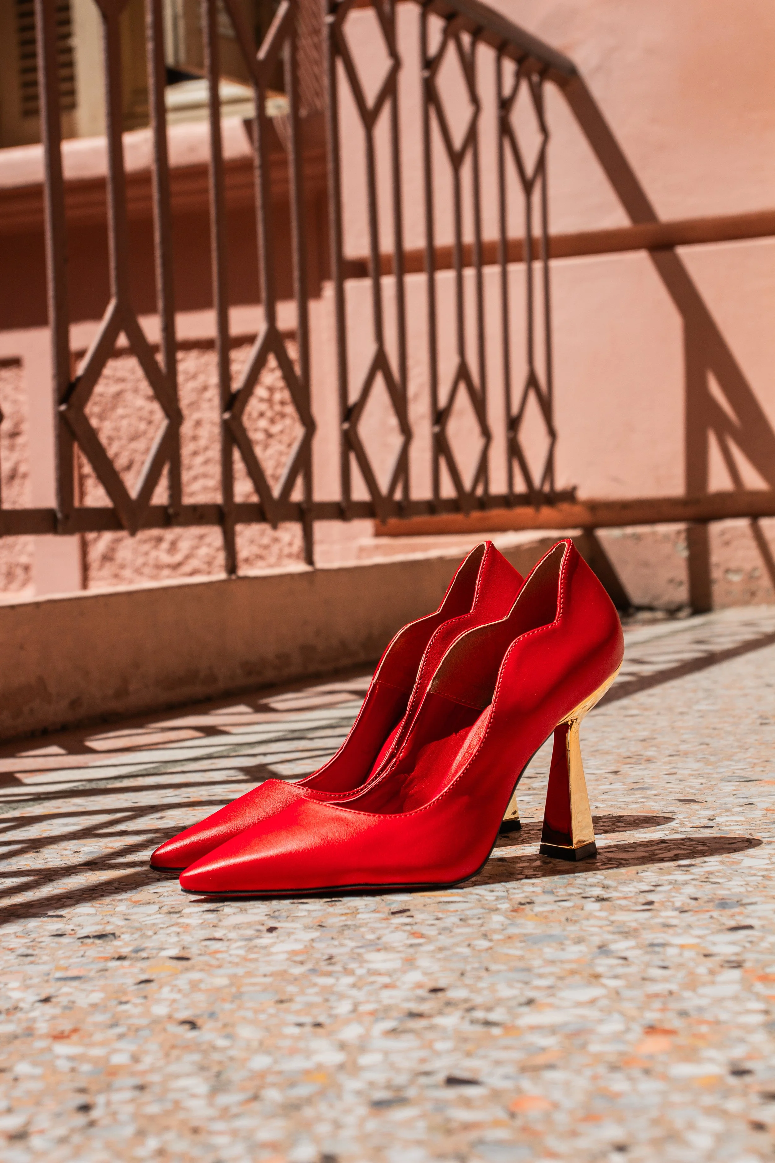 Sapatos vermelhos de salto alto em um piso de pedra, ao lado de uma escada com guarda-corpo de metal.