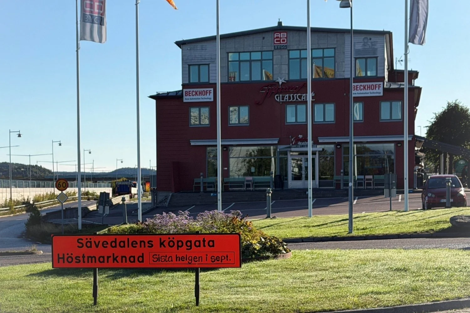 Orange vägskylt på en gräsmatta med texten ”Sävedalens köpgata – Höstmarknad, sista helgen i september”.