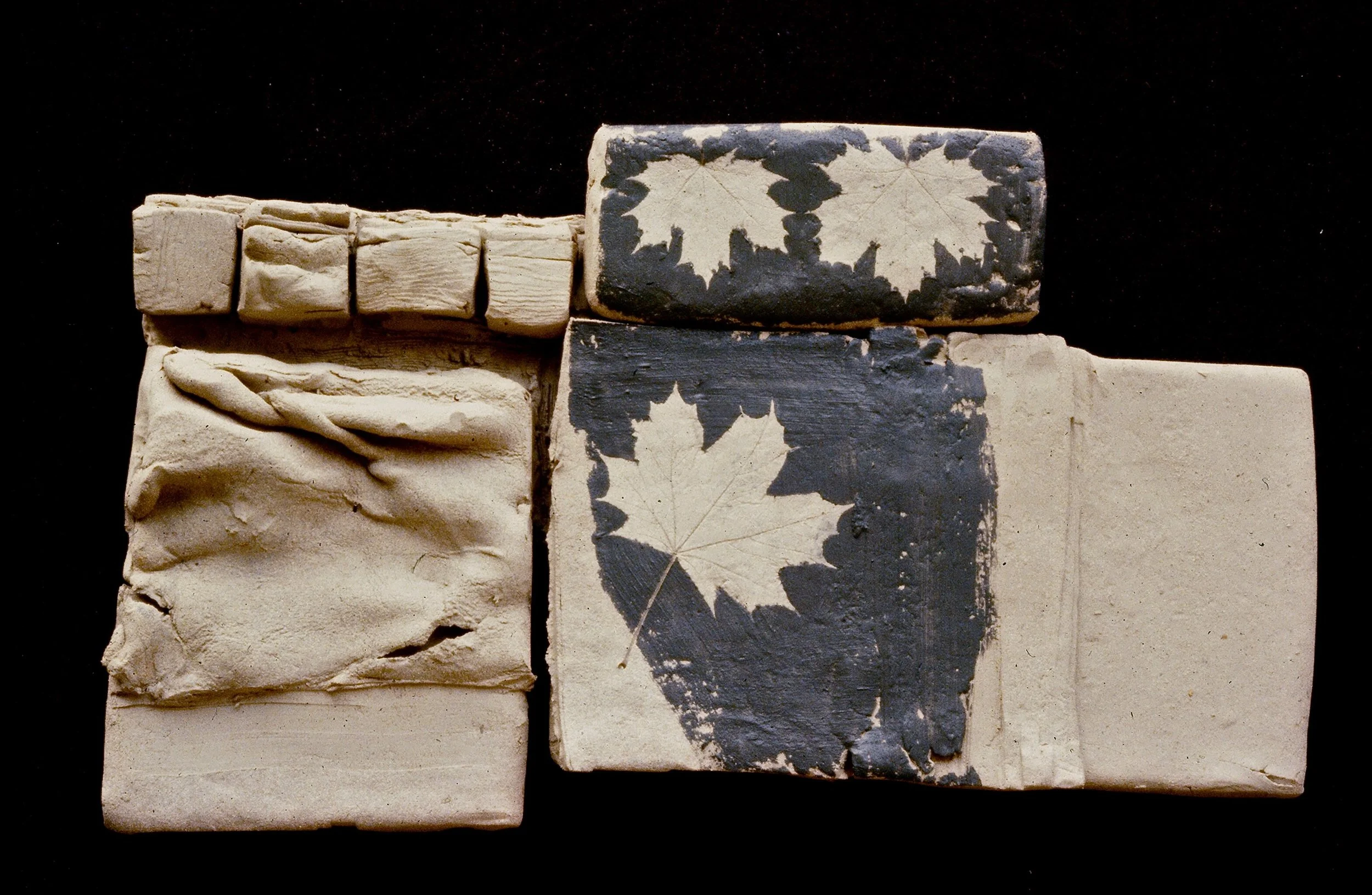 A collection of small ceramic tiles, some with leaf patterns and others with textured or plain surfaces, arranged against a black background.