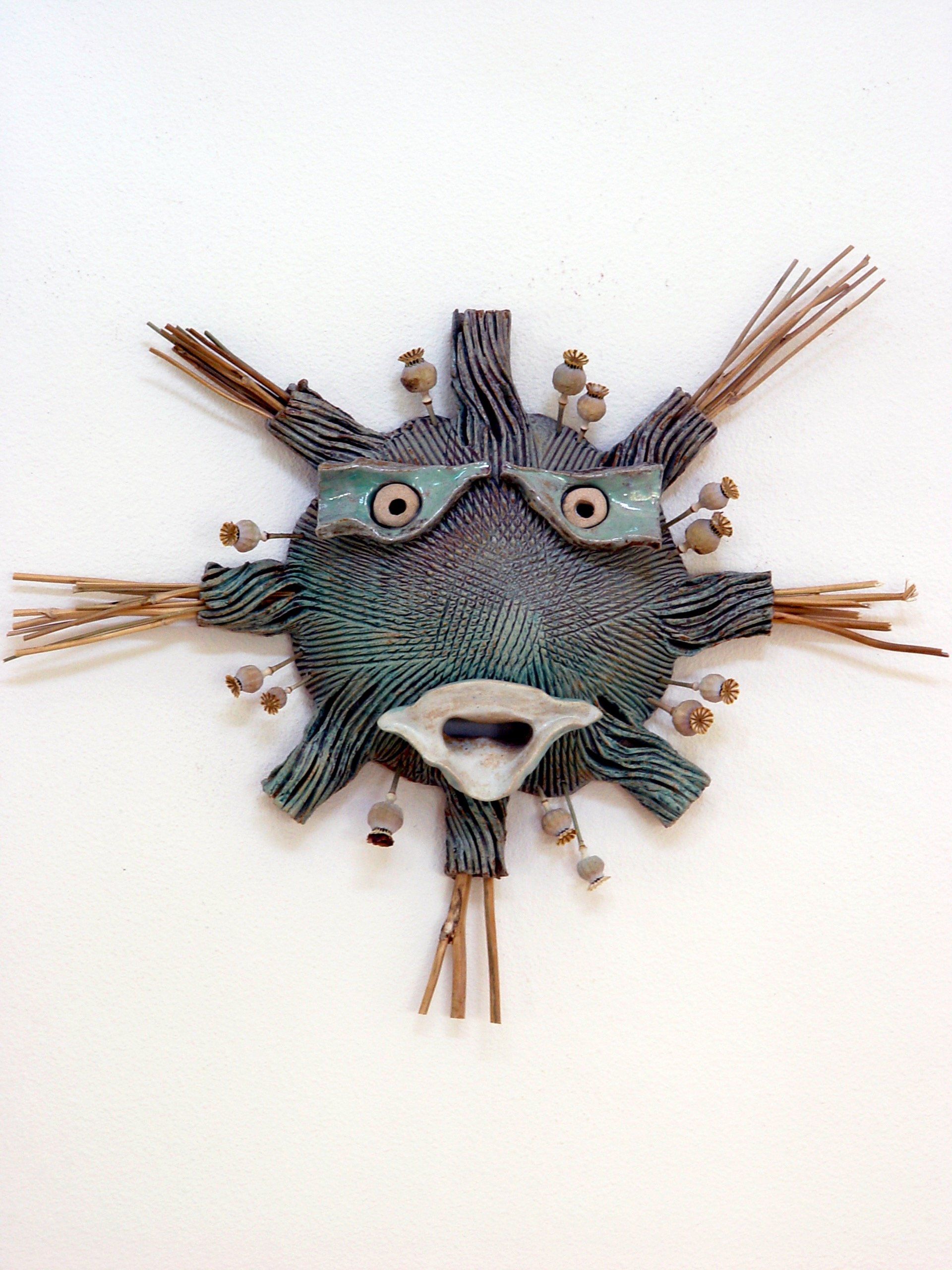 A decorative wall art piece resembling a stylized animal face made of ceramic and natural materials, with straw elements extending outward.